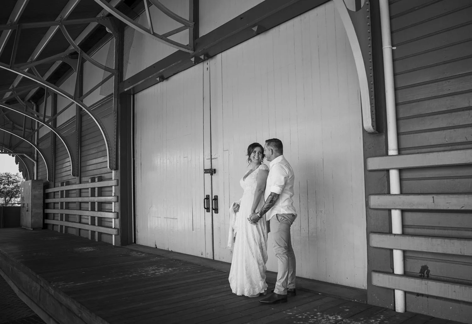 Black-and-white portrait of a couple beneath a huge industrial wharf shed