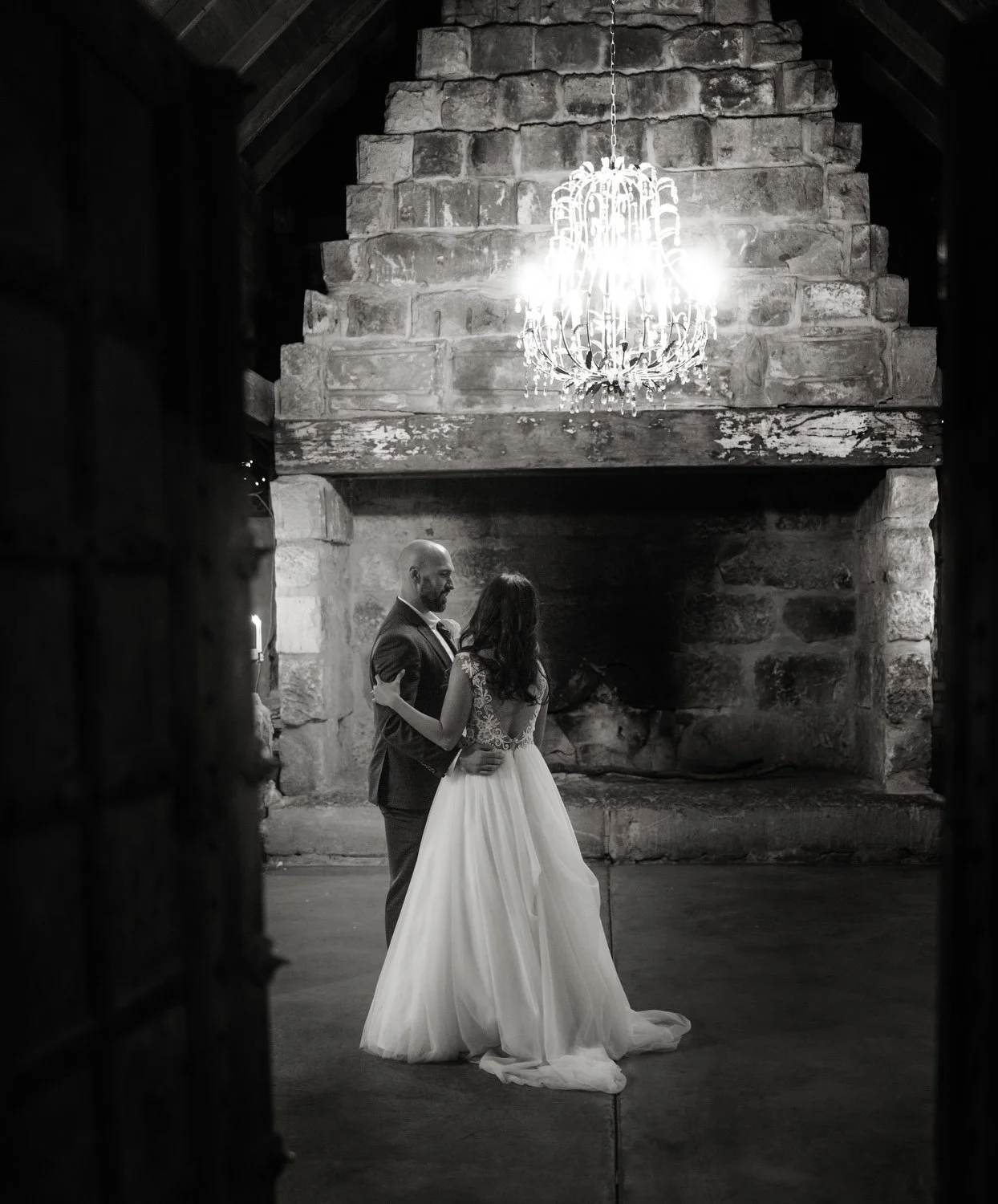 black and white image peeping through wooden doors of Peppers Creek Barrel Room  with Bride and Groom dancing 