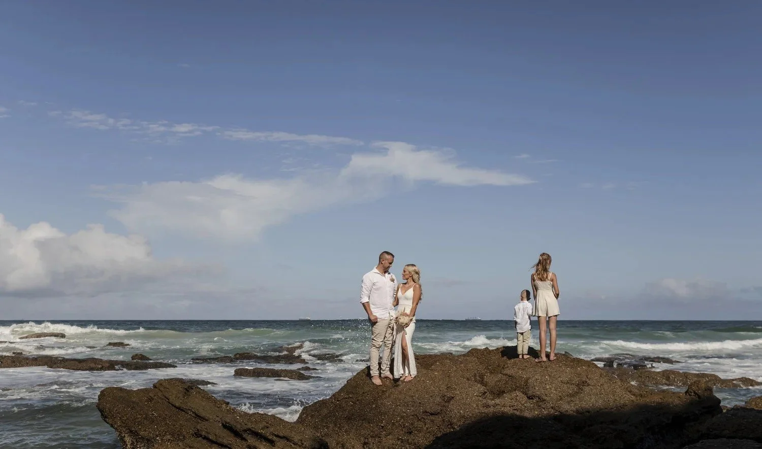 Family standing on a rock shelf by the ocean at Caves Beach