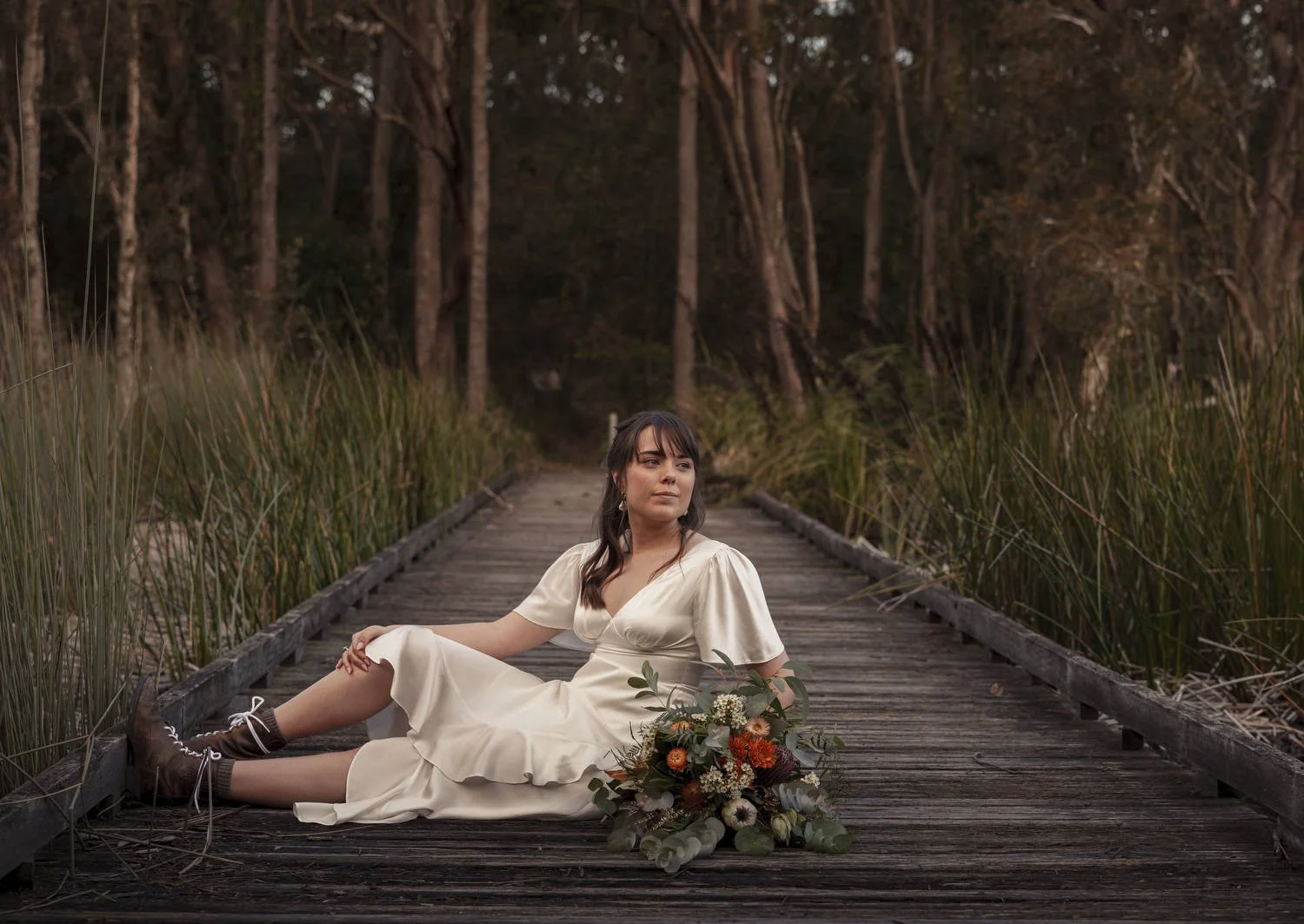 Bride reclining on a timber boardwalk with her bouquet at a Newcastle wedding