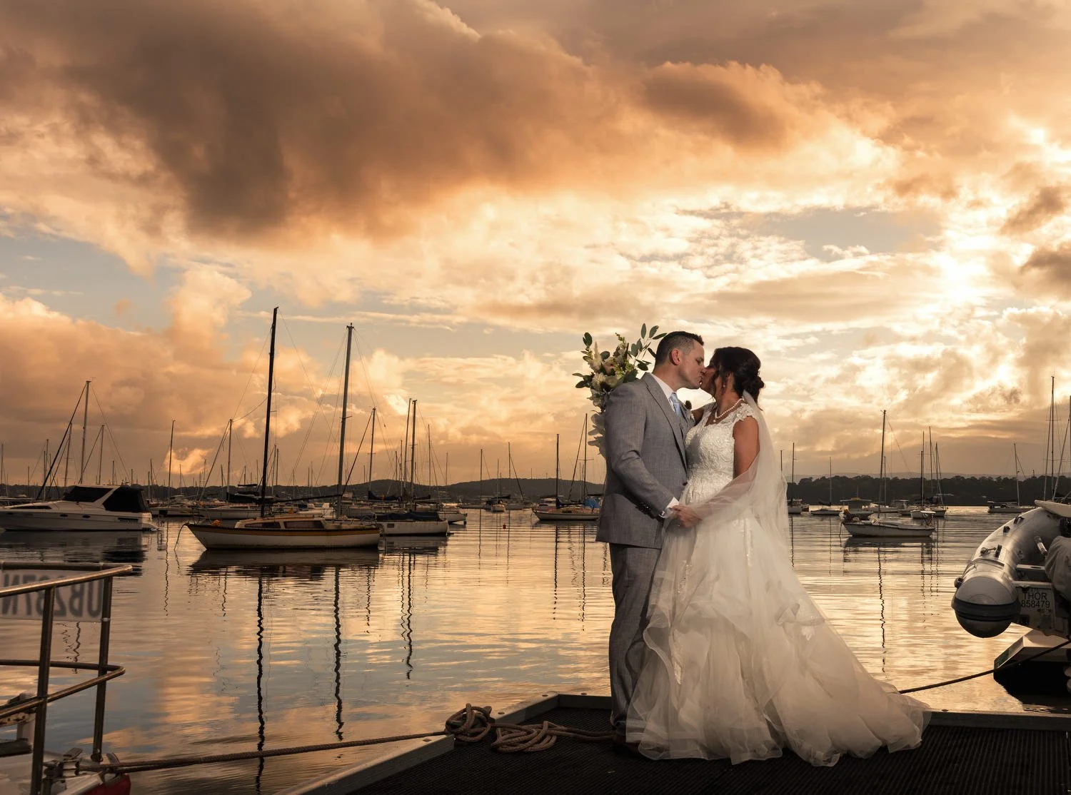Couple embracing on a jetty with moored yachts under fiery sunset clouds, Lake Macquarie