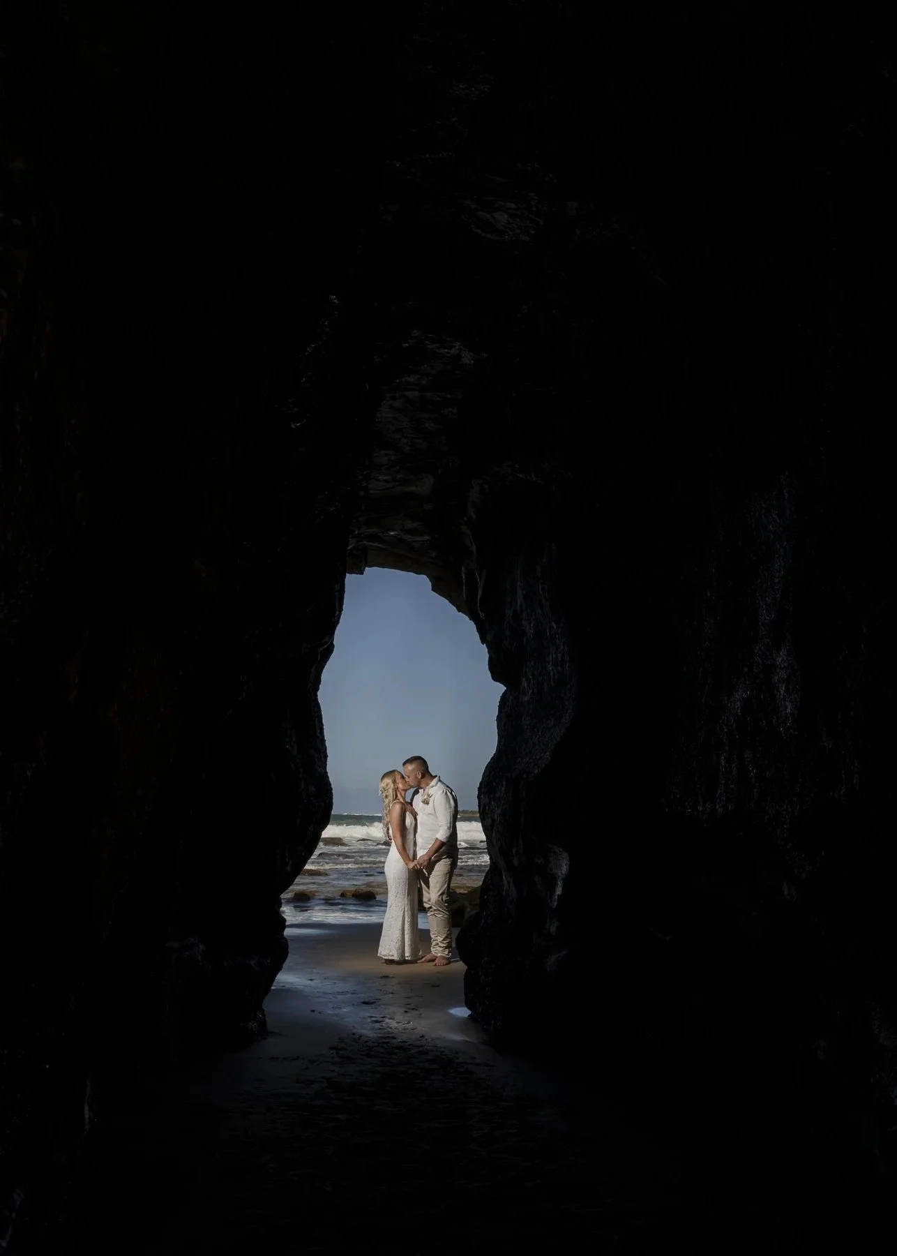 Couple silhouetted in a sea cave opening looking out to the ocean