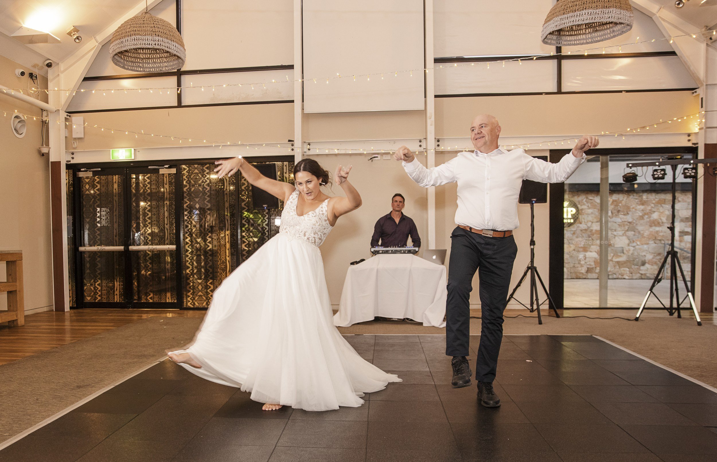 Bride and a guest dancing playfully on the reception dance floor under festoon lights