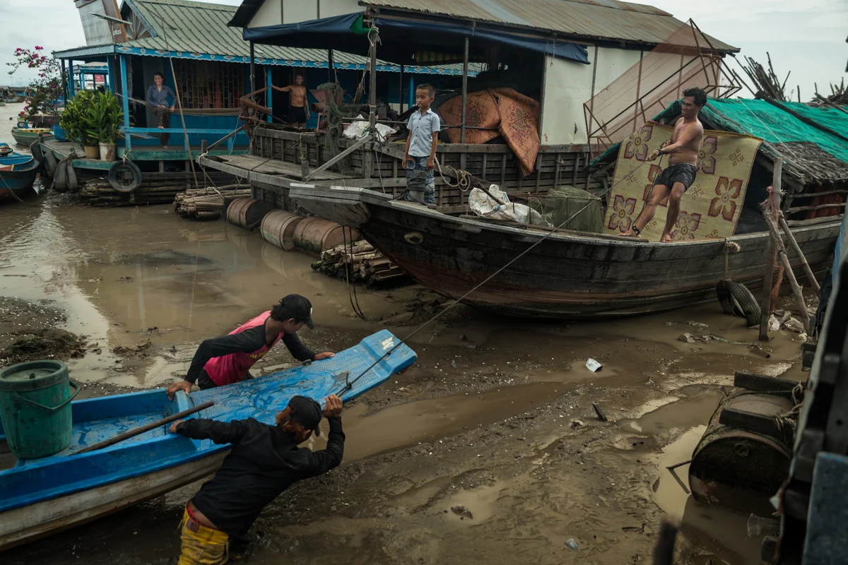 May 26, 2016 - Kampong Loung, Cambodia. A boat carrying goods is pushed up towards a storage barque. When the afternoon winds come from the east water levels drop on Kampong Loung making many floating homes only accessible by wading through deep mud. © Nicolas Axelrod / Ruom