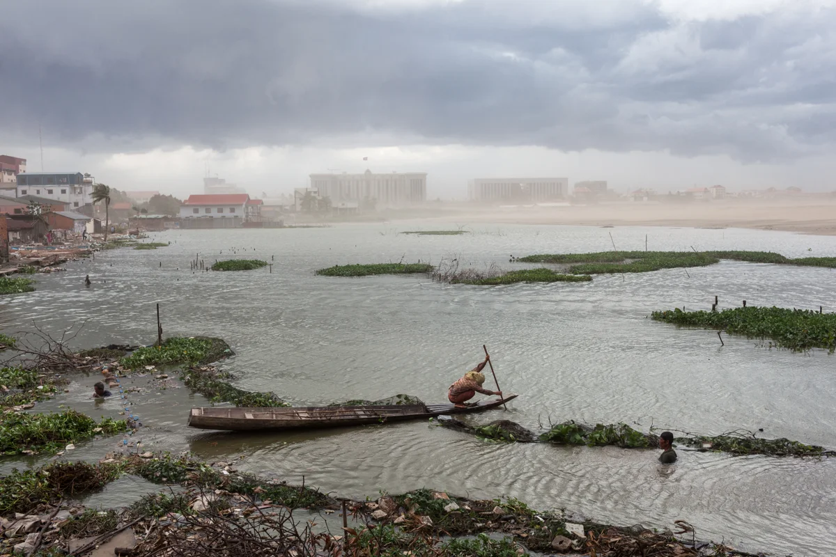  July 07, 2011 - Phnom Penh, Cambodia. A woman paddles her boat against an a storm on Boeung Kak lake. The new buildings of the Council of Ministers and the office of the prime minister can be seen in the background. The lake was reclaimed to make way for residential and commercial complexes. � Nicolas Axelrod / Ruom 