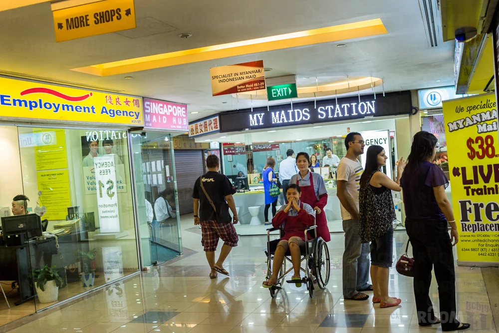 March 24, 2014 - Singapore. Maid agencies at Katong shopping centre. The girl in the wheel-chair is a domestic helper and is being pushed around the hall by another domestic helper in front of a maid agency to promote the work the agency. © Nicolas Axelrod / Ruom
