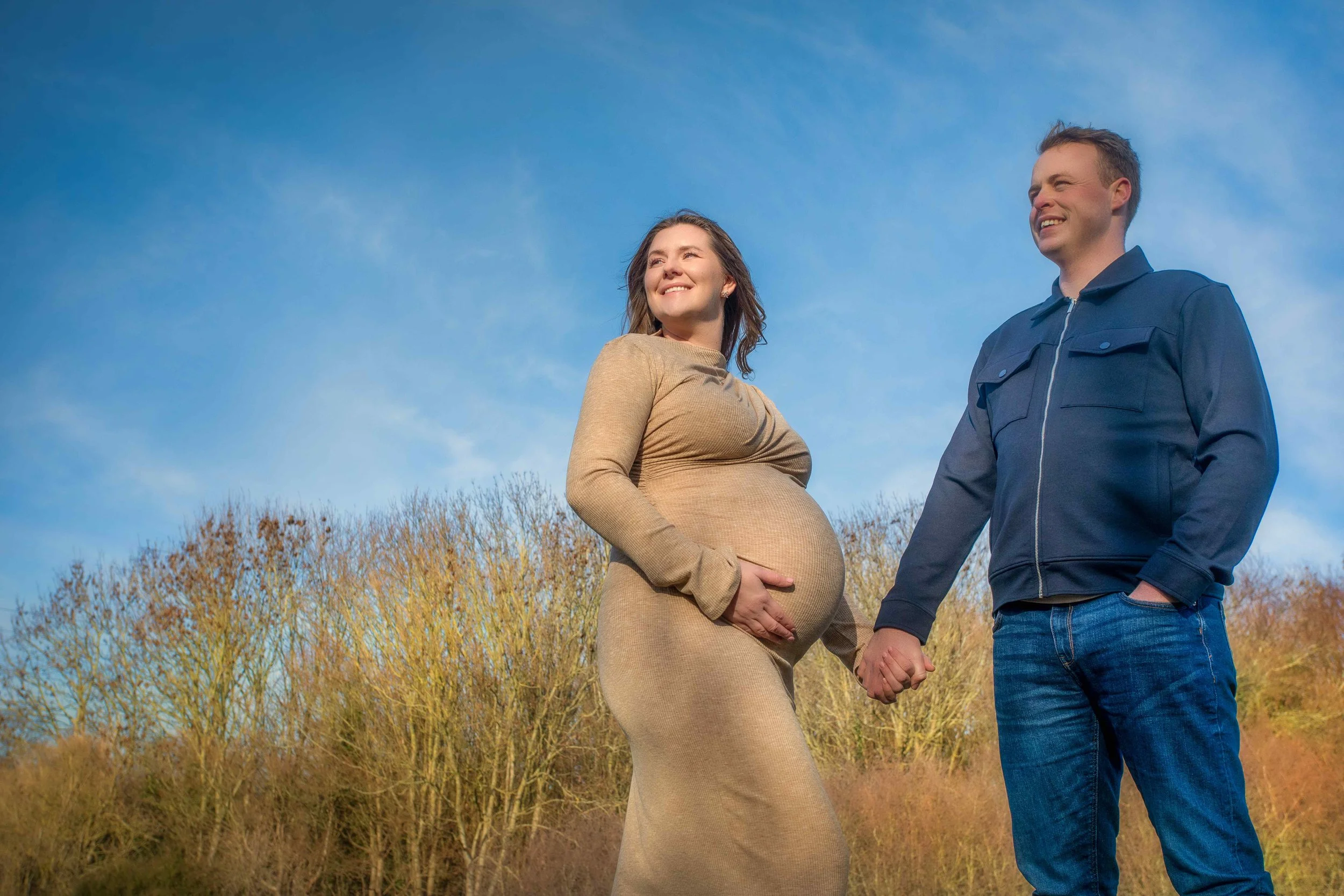 outdoor-maternity-shoot-couple-holding-hands-blue-sky.jpg