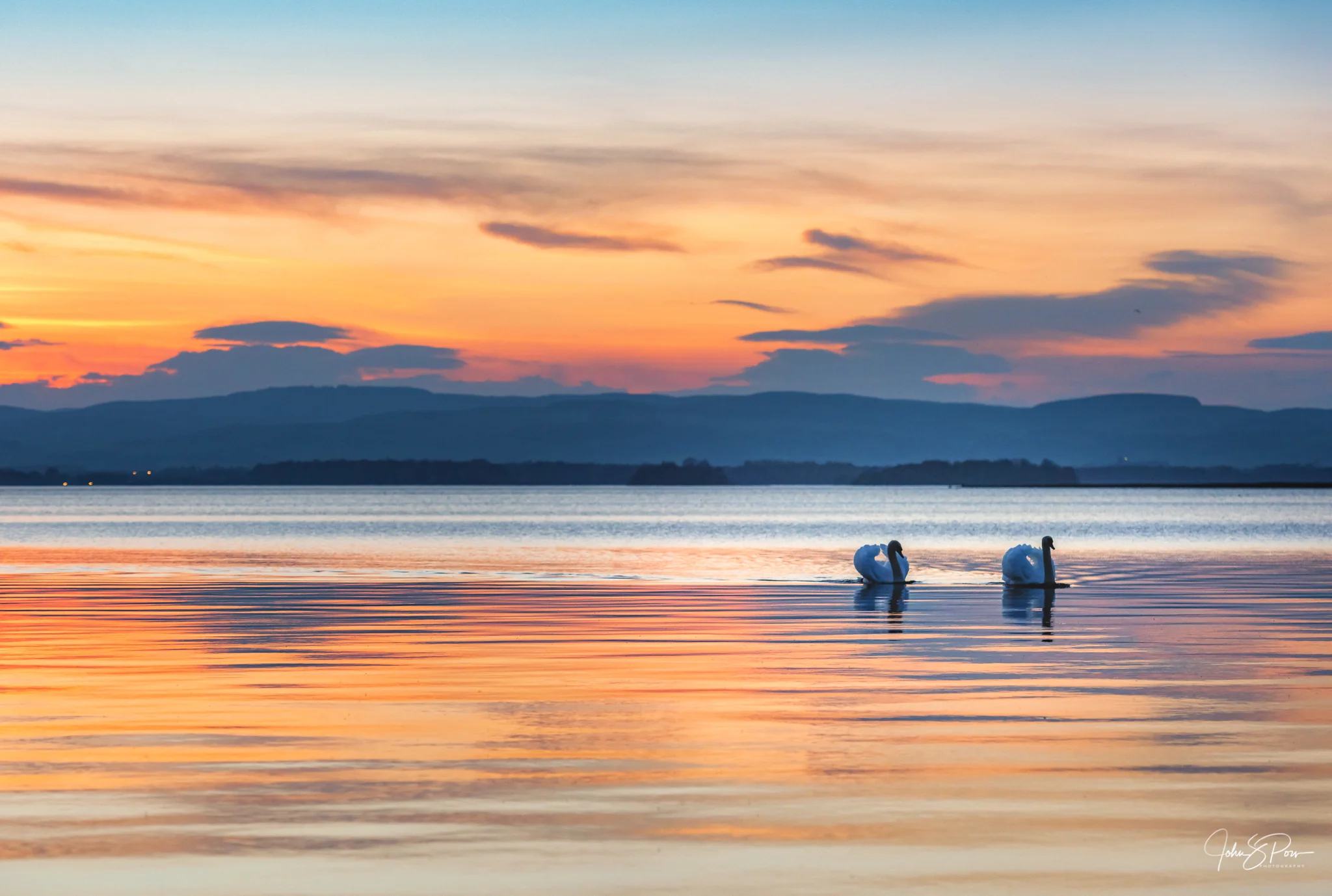 Two swans swimming in Loch Leven at Sunset. The swans are placed at the intersecting point a third of the way up from the bottom of the image and a third of the way in from the right. The horizon is in the middle of the image, but it is just one of a number of horizontal lines, so it does not split the scene.