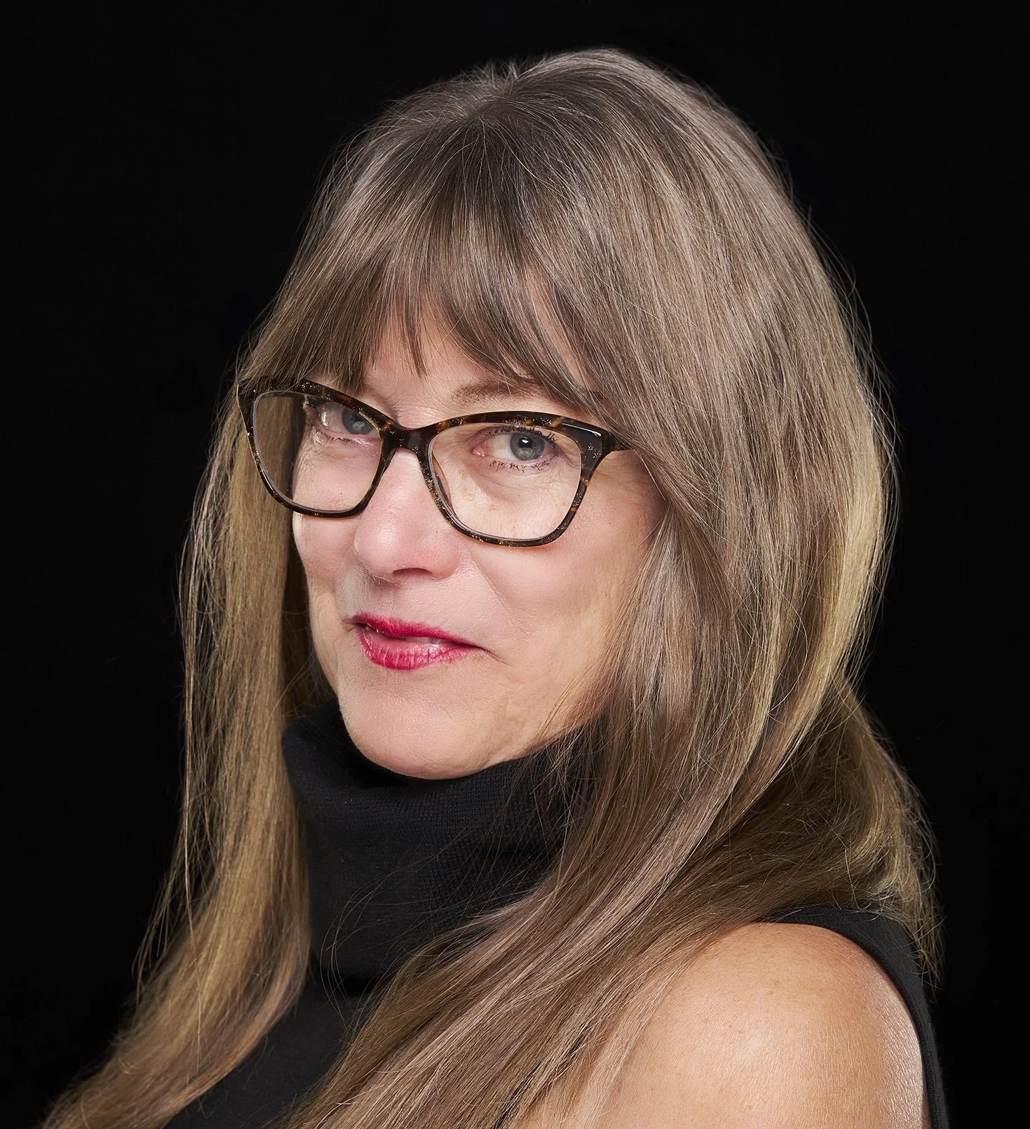 Author photo of Mary Dezember. Woman with glasses, bright eyes, long hair, head turned to viewer.