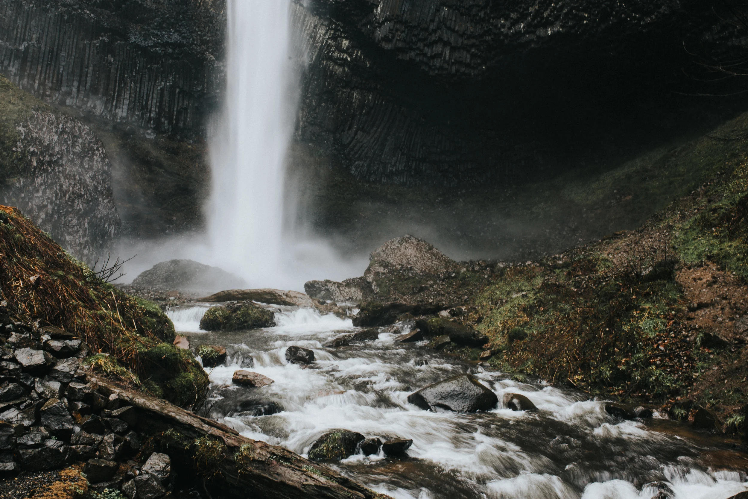 Waterfall cascading into a river with rocks and moss-covered terrain in a forest setting.