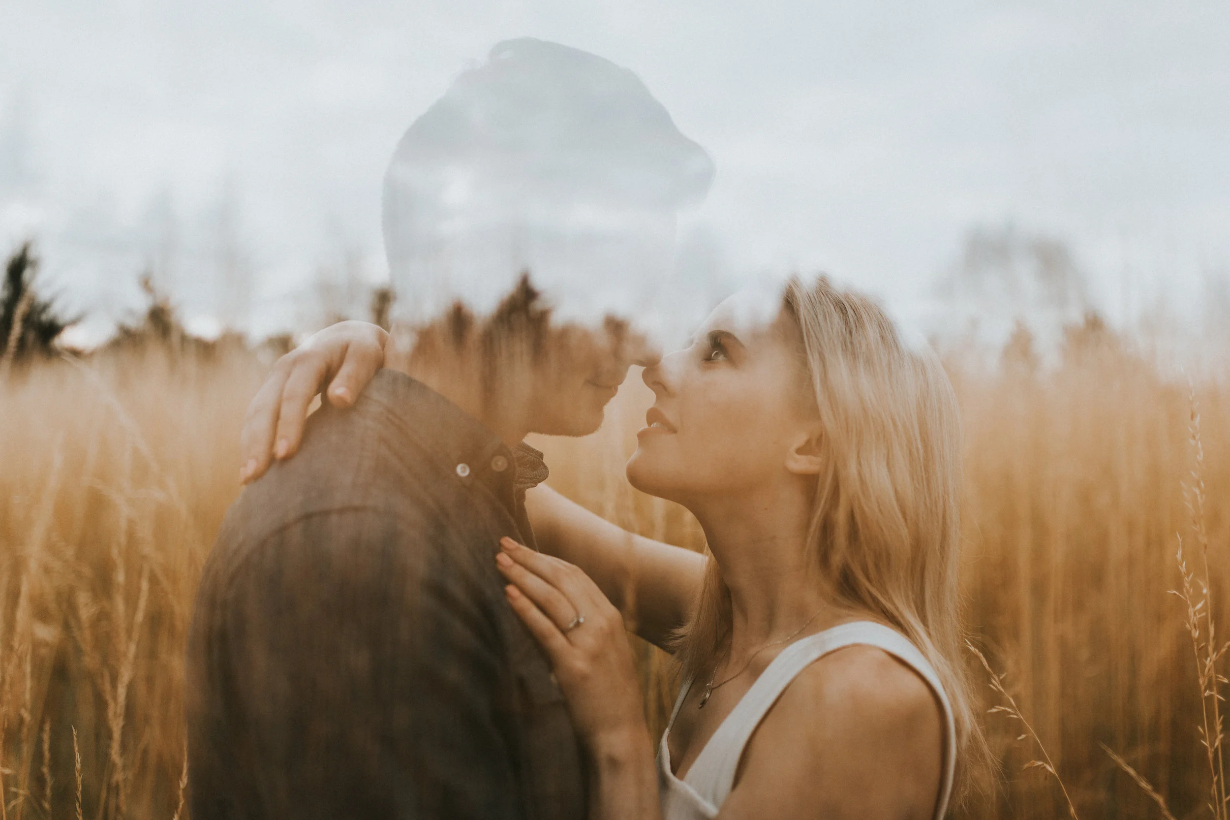 A couple sharing a romantic moment in a field of tall, golden grass, with nicknames touching nose to nose, under an overcast sky.