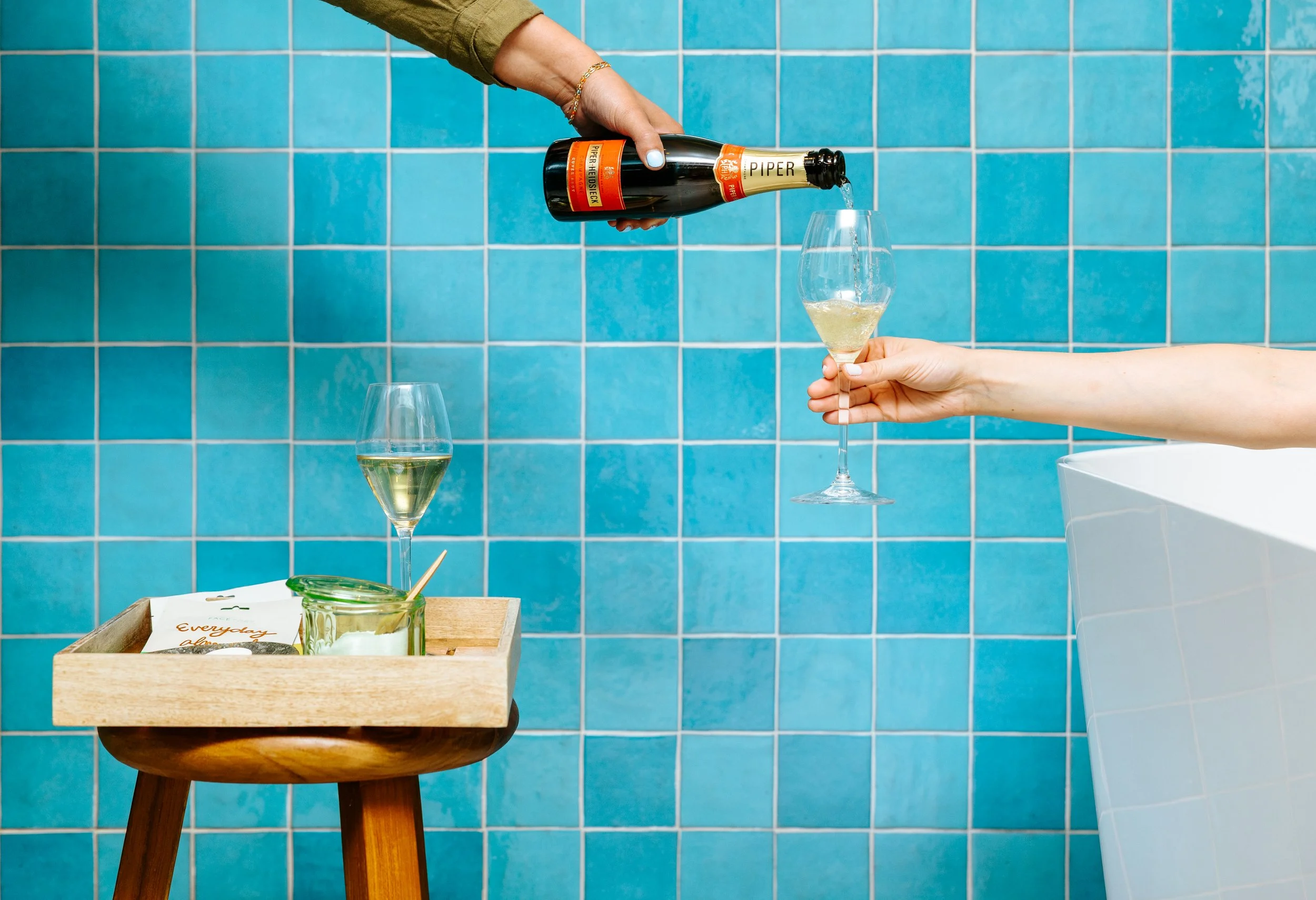 Person pouring champagne into a glass in a blue tiled room.