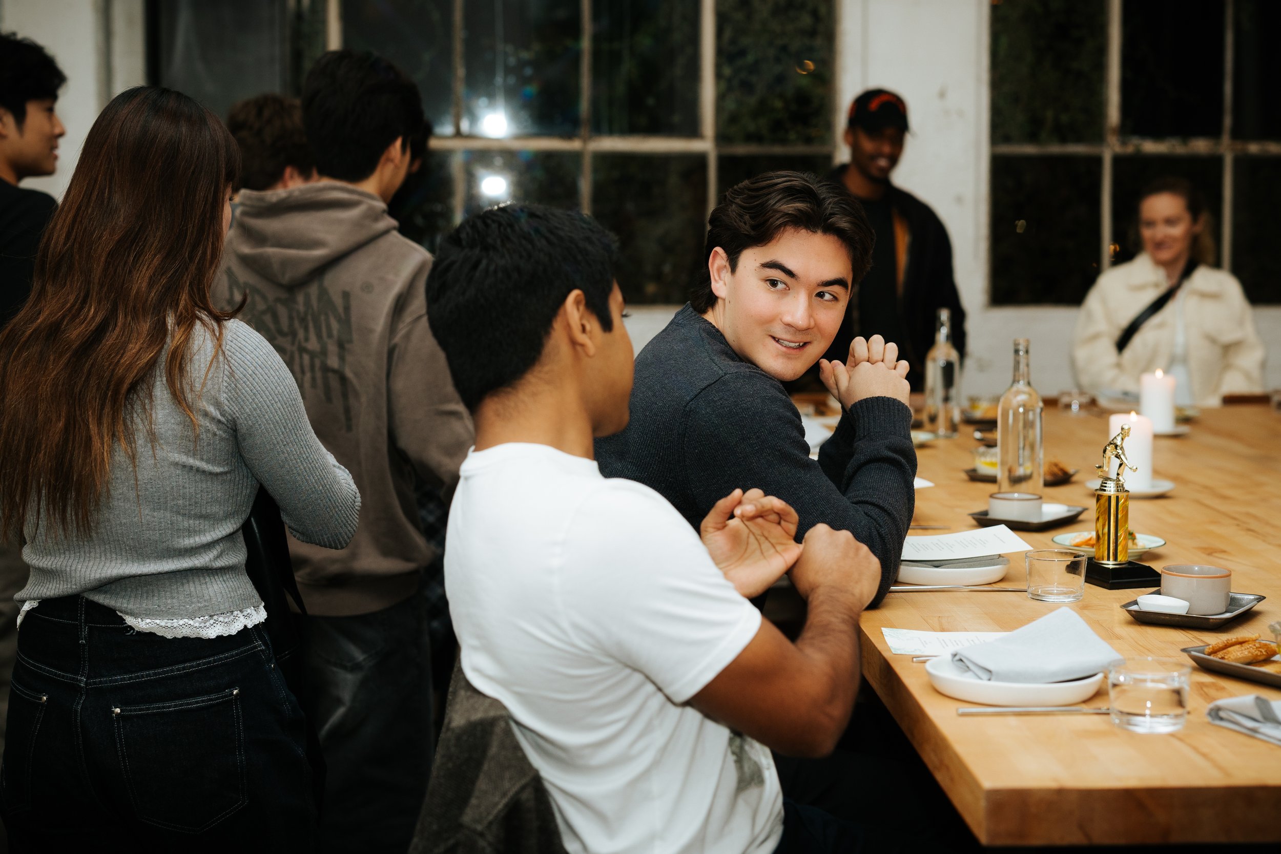 People gathered around a wooden table in a restaurant, with one person turned towards the camera smiling.