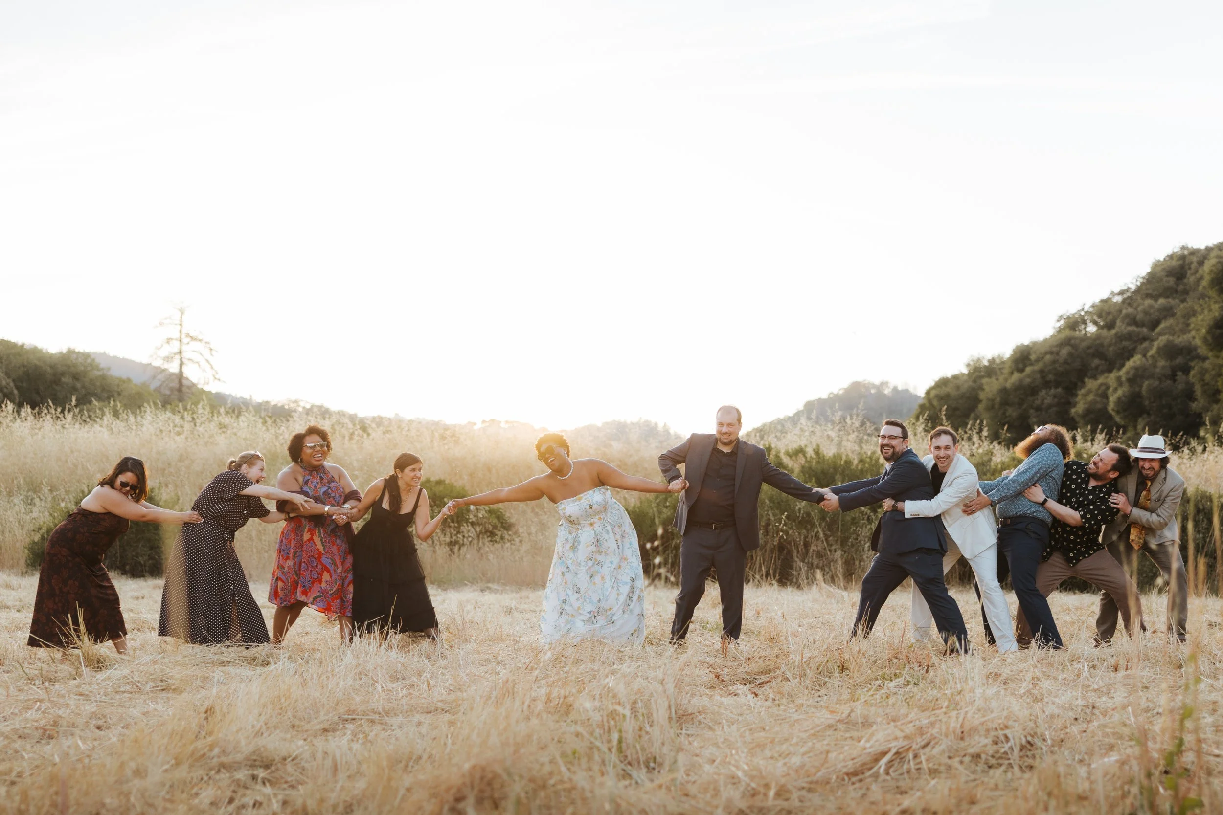 Group of diverse people holding hands in a meadow during sunset, forming a circle and smiling.