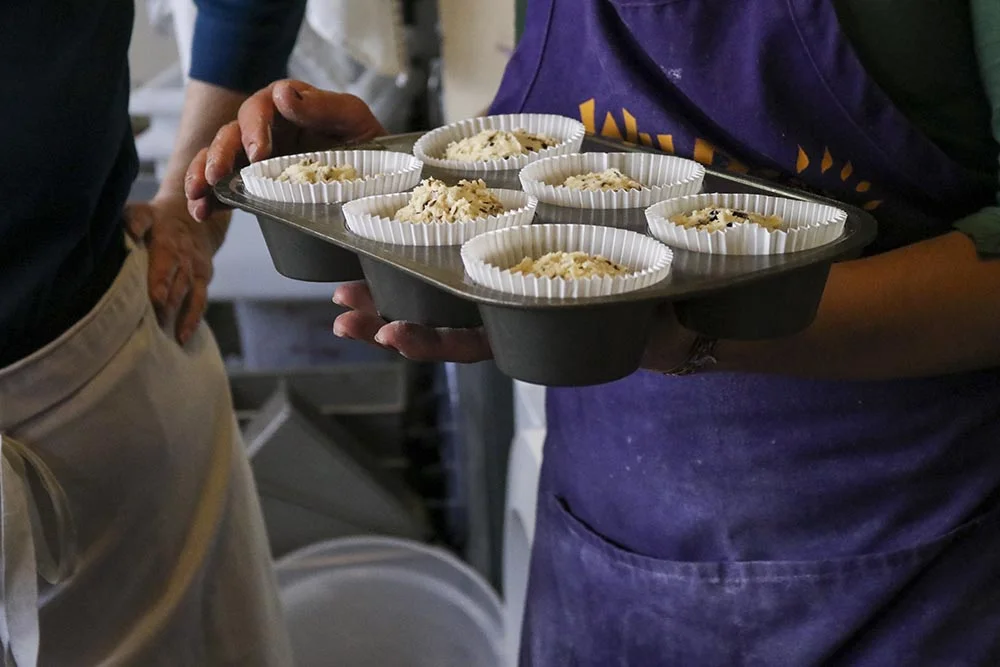 Monica talks to a baker about muffins going into the oven.
