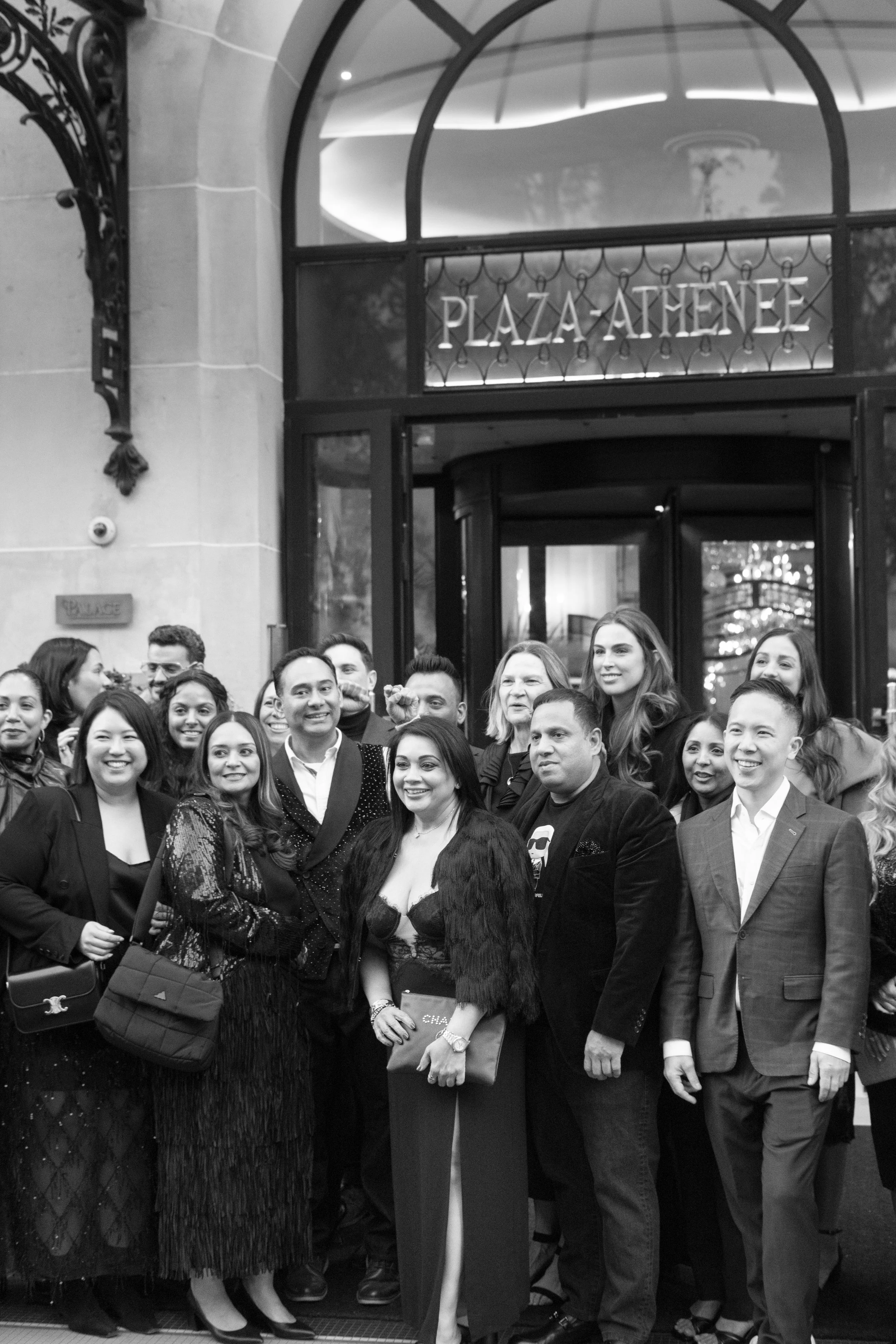 A group of diverse people in formal attire standing in front of a building with a sign that reads 'Plaza Athenee'.