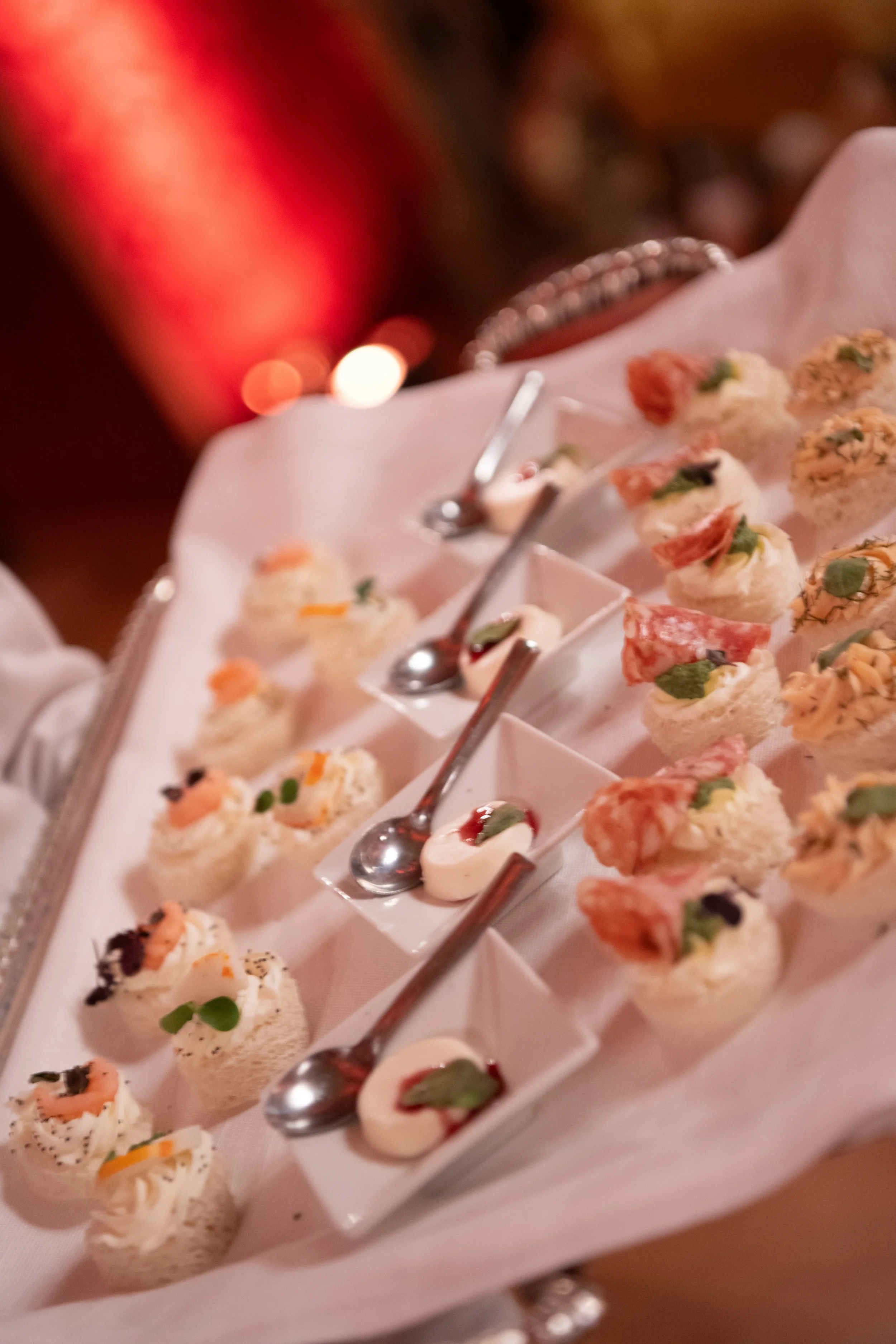 Close-up of a tray of assorted bite-sized appetizers, possibly canapés, garnished with herbs and presented on small white plates with spoons.
