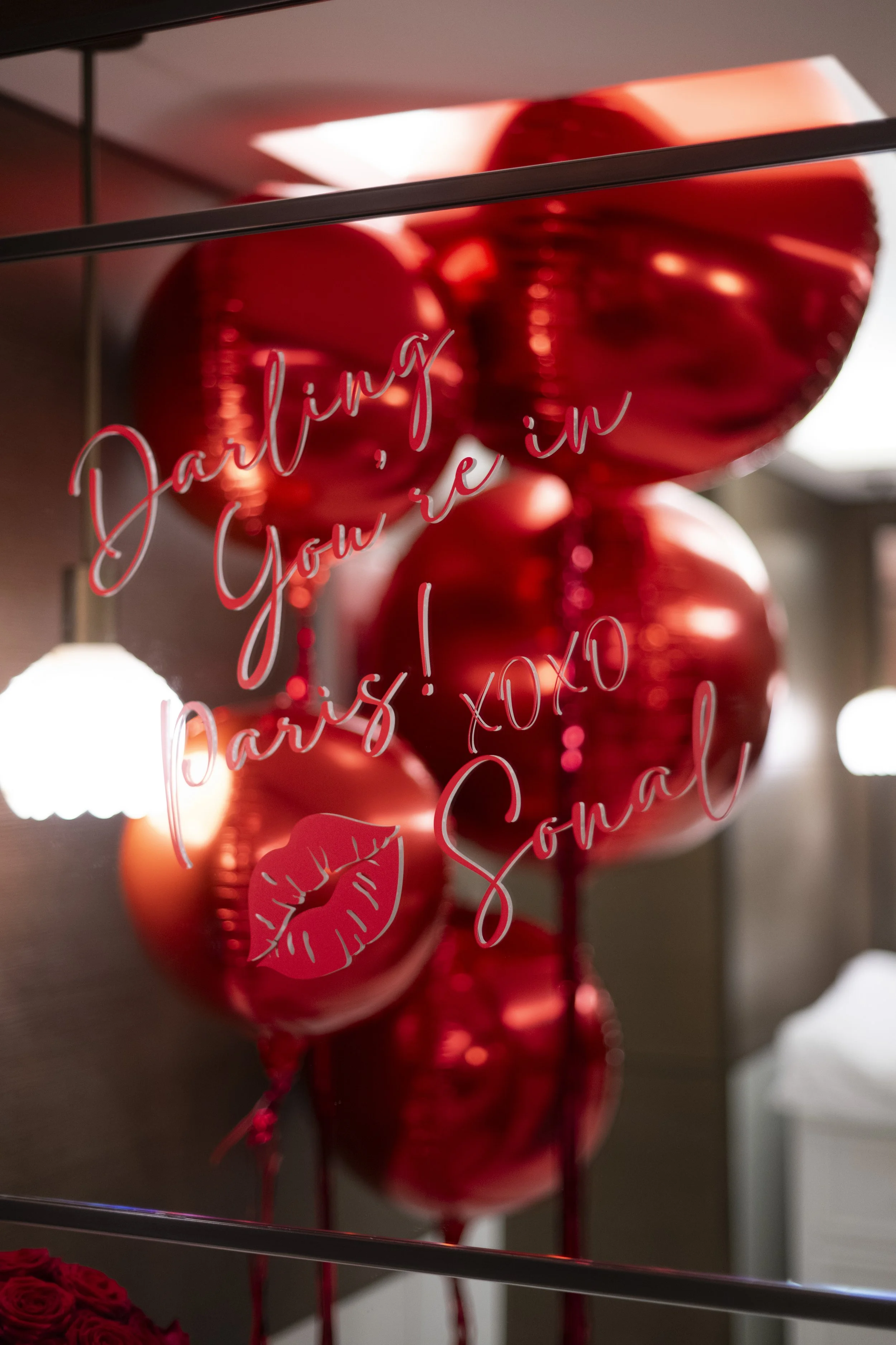 Red heart-shaped balloons and a neon sign saying "date in your arms!" with a red lipstick kiss mark on a reflective surface.