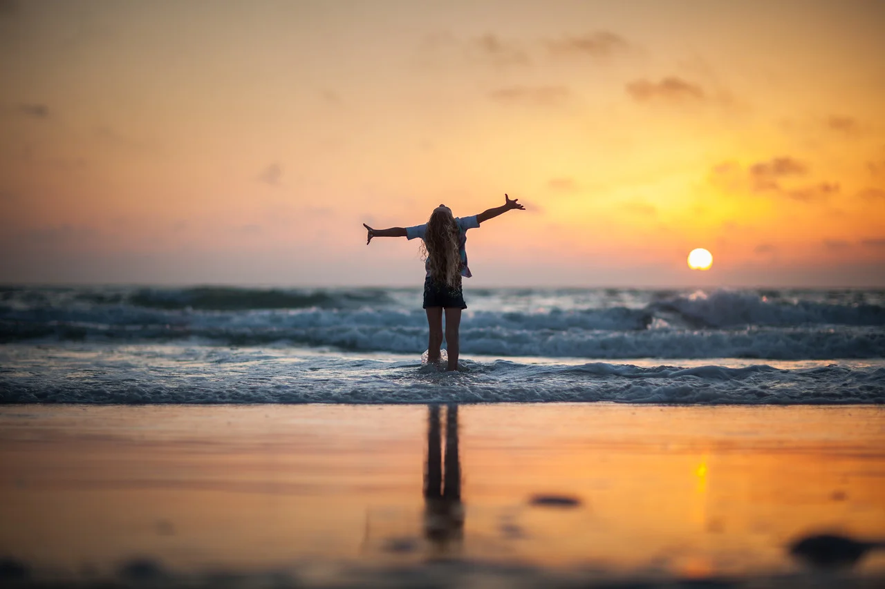 Woman-Standing-Ocean-Shore-Arms-Air-Enjoying-Sunset-X2.jpg