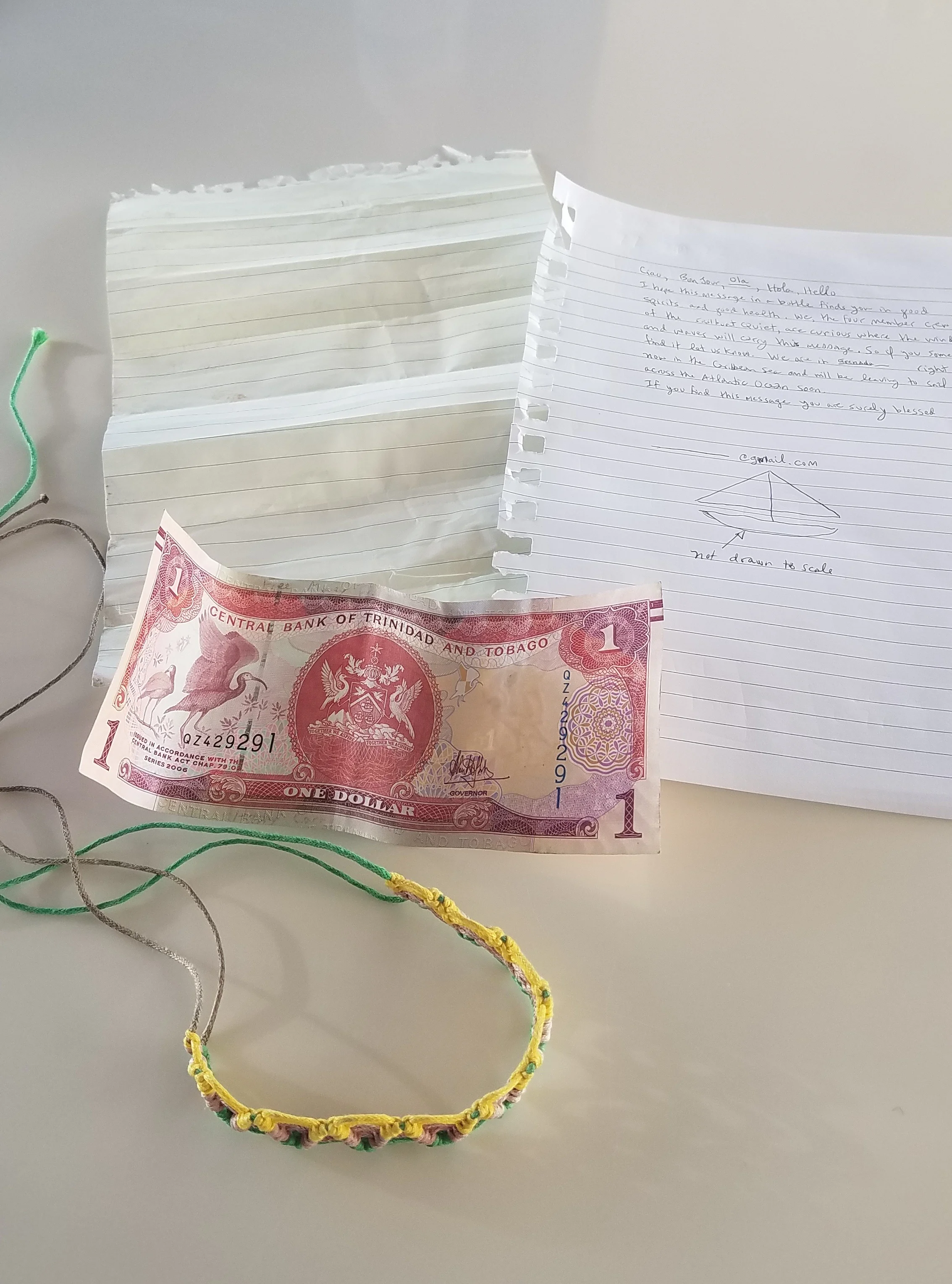 The contents of the bottle; the original faded note, the reconstructed version of the note, the dollar from Trinidad & Tobago and the bracelet