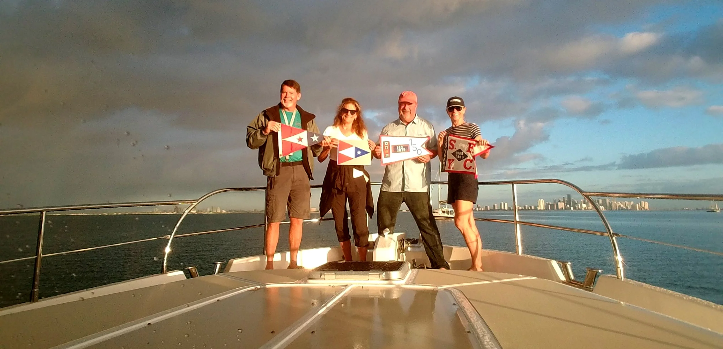 The ‘Burgee Brigade’ on the deck of The Independence in front of the Miami skyline, Biscayne Bay, FL. Larry holds the SFYC burgee, Kappy - the 150 Anniversary Book, Mark - our 150 year anniversary burgee & Jamie - the 120 year anniversary burgee