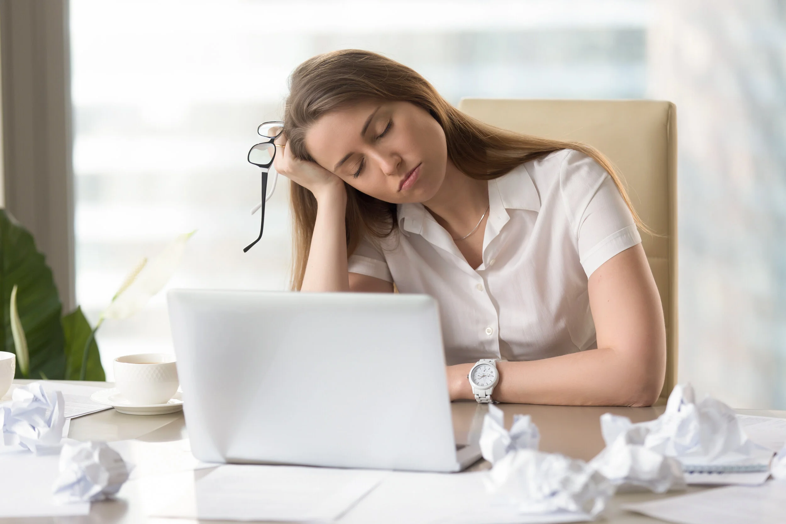 Businesswoman sleeping with head on hand at the desk. Sleepy girl dozing at workplace. Tired female office worker suffering from lack of sleep. Lazy girl bored routine. After-hours work in office