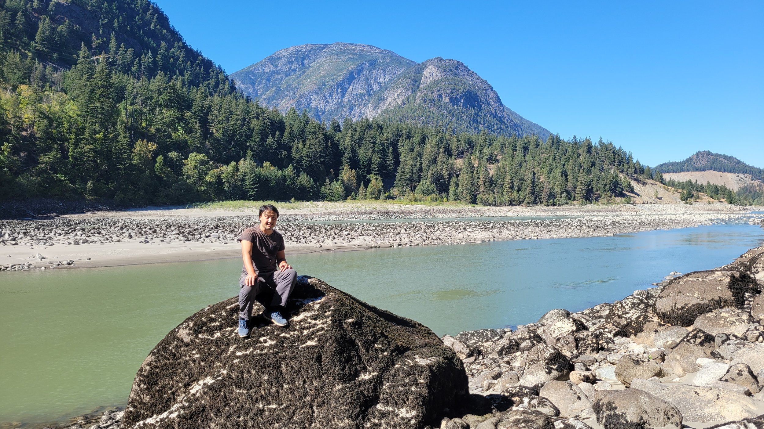  Ken Wu, co-founder of the Nature-Based Solutions Foundation sits on a giant boulder by the Fraser River across from the Kwoiek Valley, part of the Kanaka Bar's Indigenous Protected and Conserved Area (IPCA) proposal - viewed here from the Old Man Ja