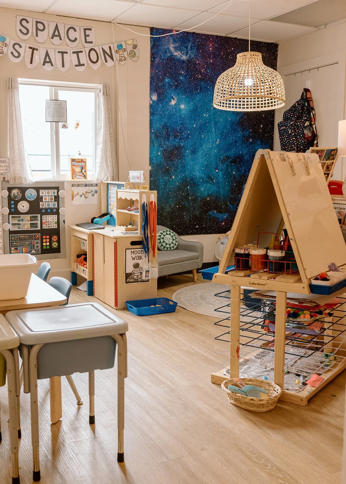 A children's playroom with a space-themed mural on the wall, a sign that reads 'Space Station,' and various toys and activity stations.