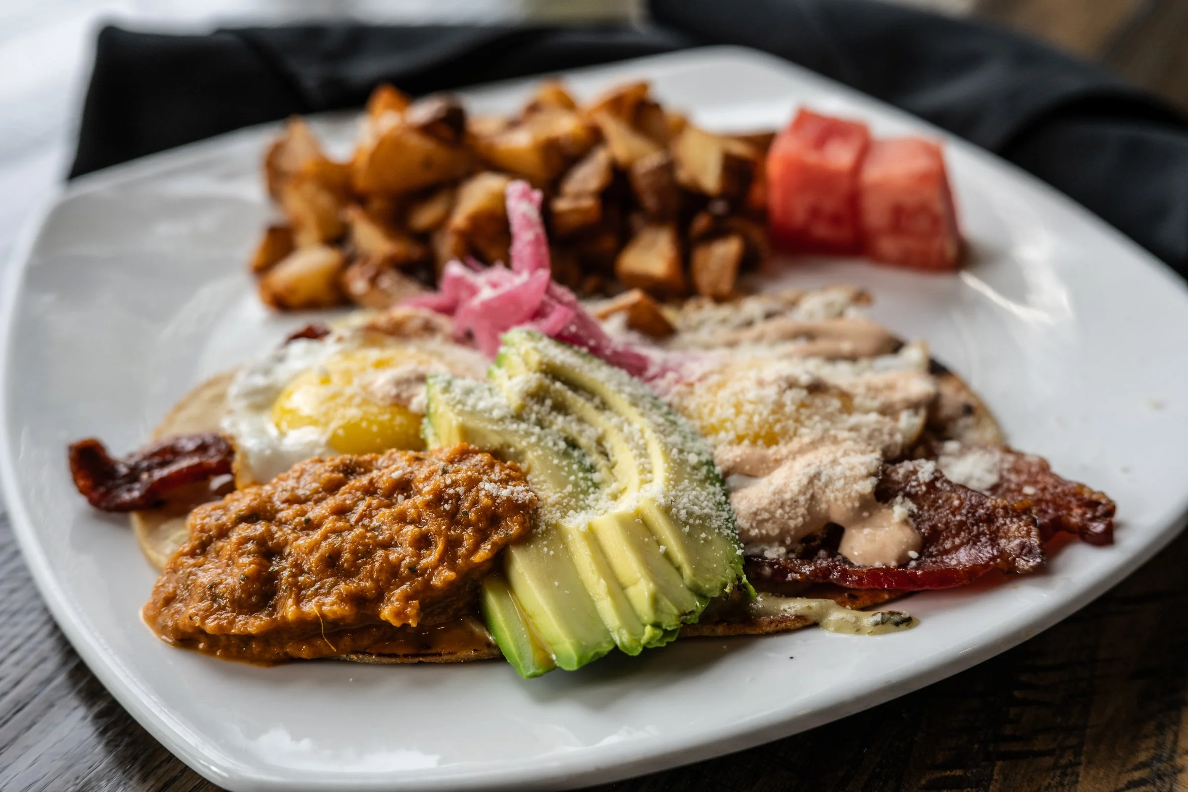 crisp corn tortilla, sunny-side-up eggs, verde cream sauce, bacon, avocado, chipotle crema, pickled onions, cotija cheese, herb roasted potatoes, roasted tomato salsa
