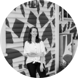 Woman standing in front of a mural with geometric patterns, smiling, wearing a white blouse.