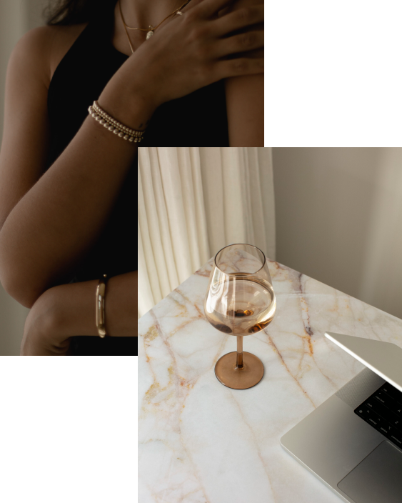 Close-up of a woman's arm wearing a bracelet, with a glass of rosé wine on a marble table and a laptop nearby