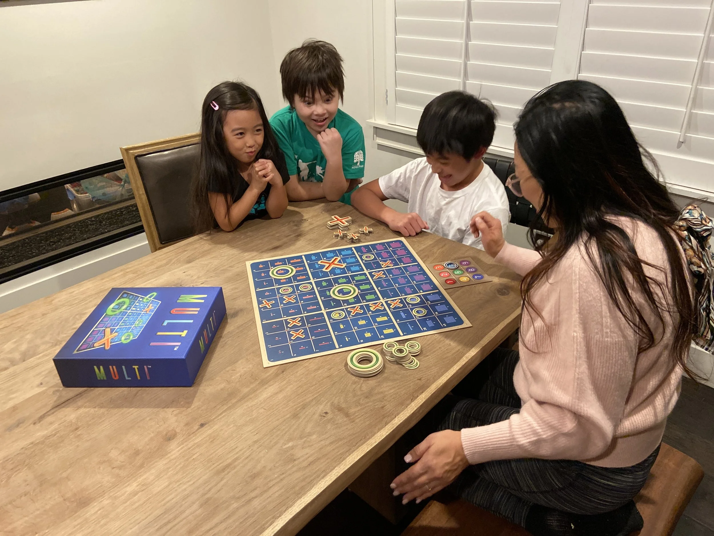 A woman plays Multi with a kid, while two other kids look on from the side.