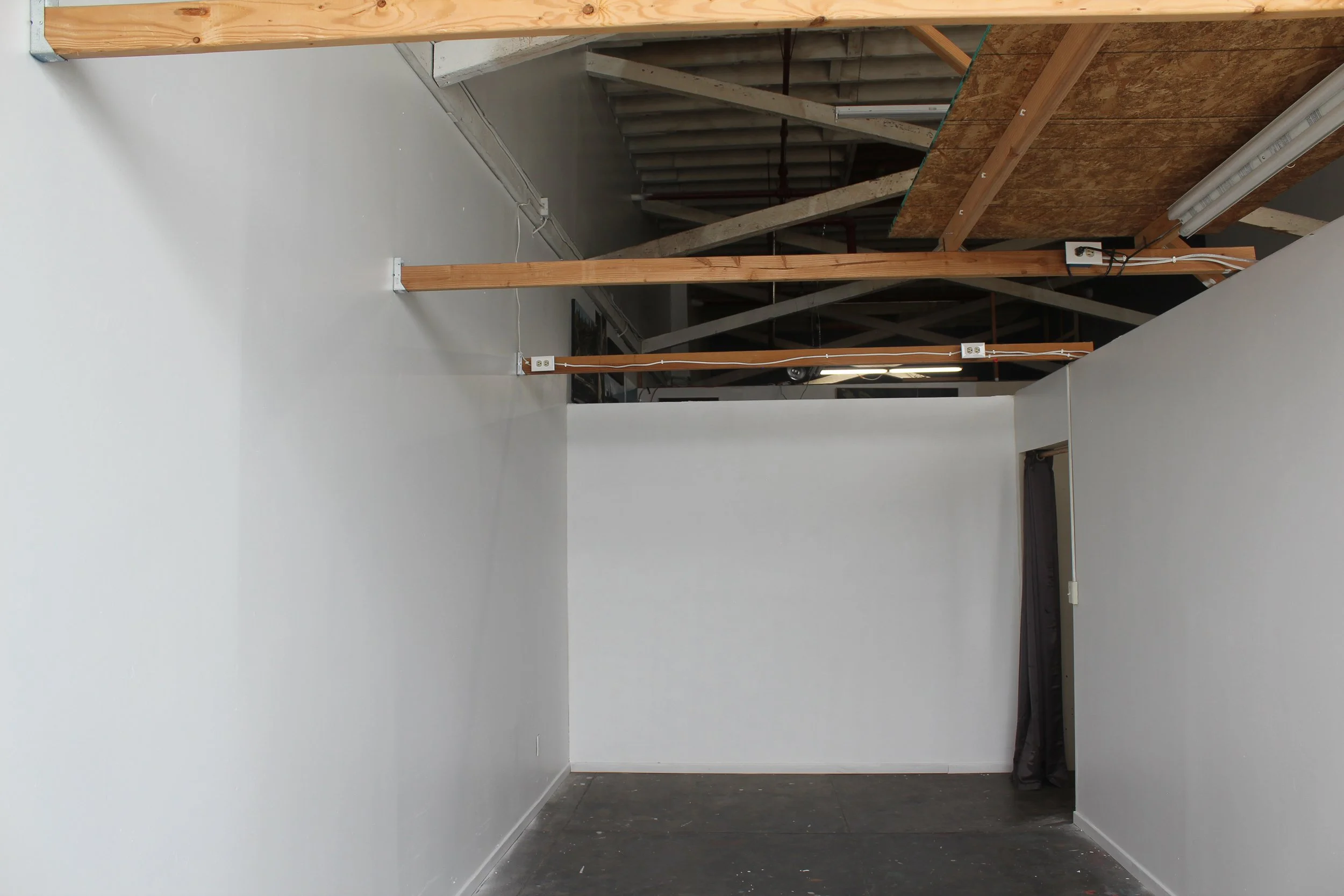 An interior space under construction with white walls, exposed wooden beams, and electrical wiring, possibly in a commercial or industrial building.