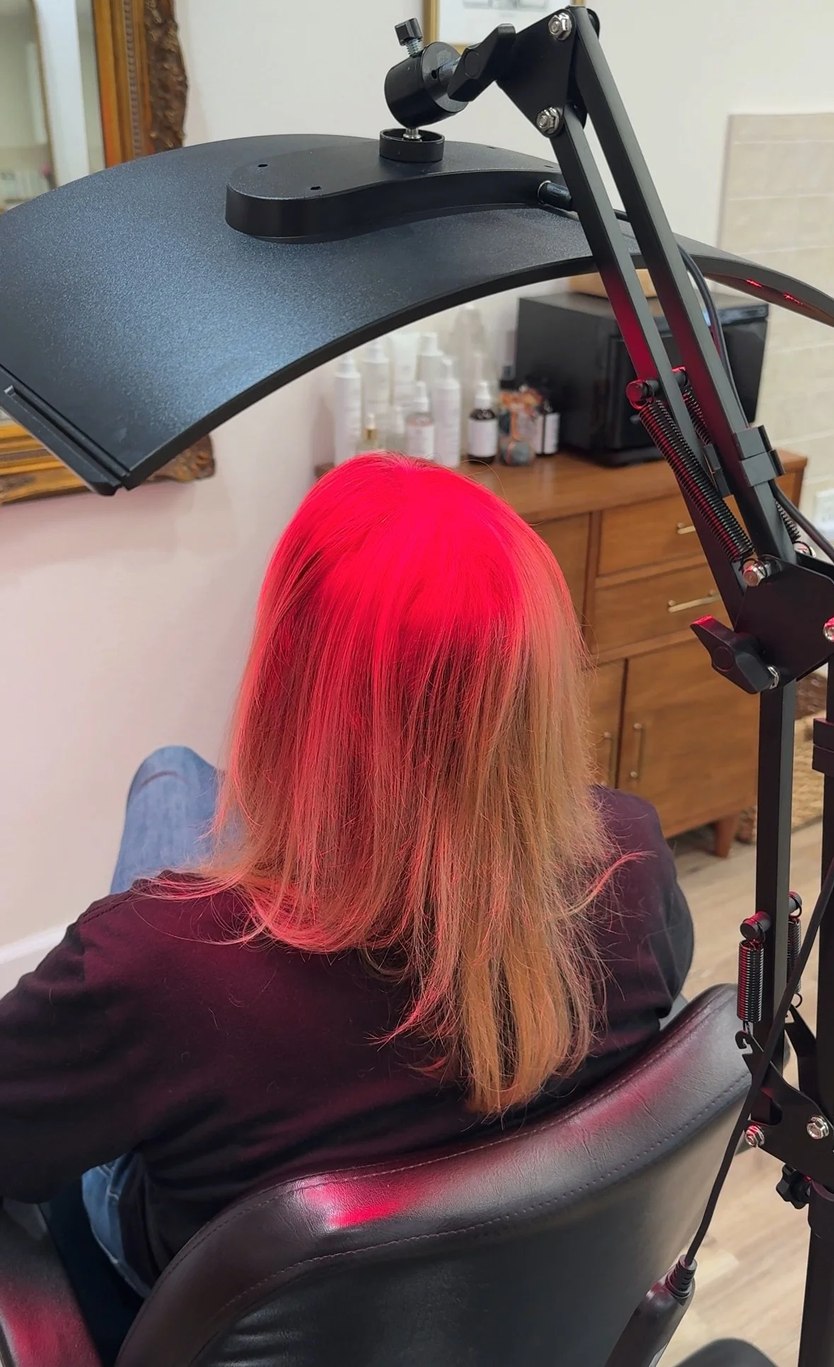 A person with long blonde hair sitting in a salon chair getting red light therapy.