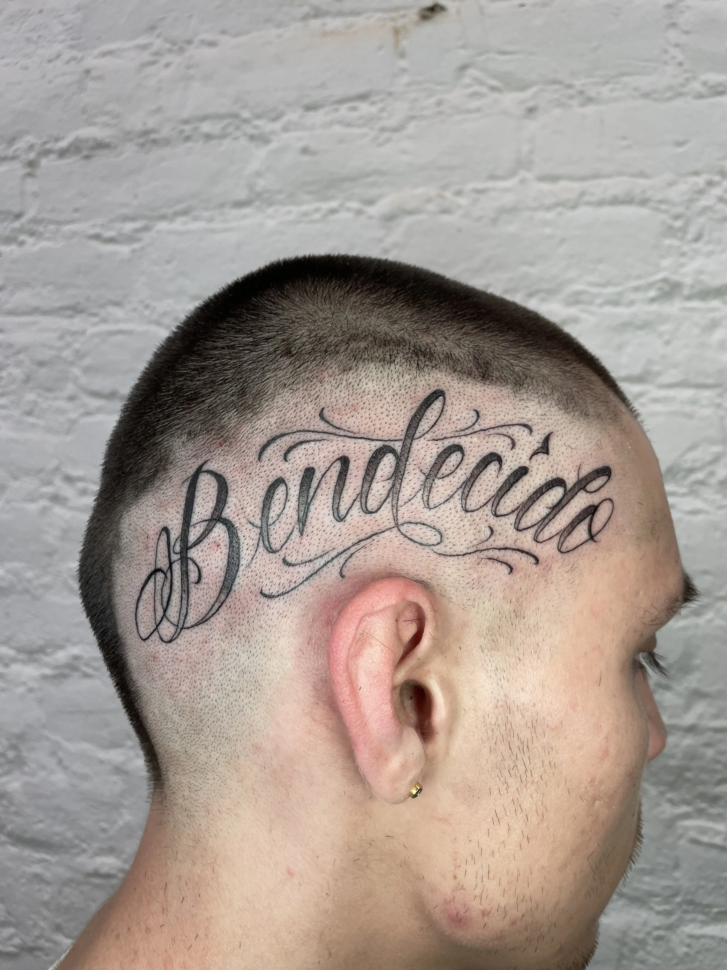letting tattoo bendecido script on the side of the head.jpeg