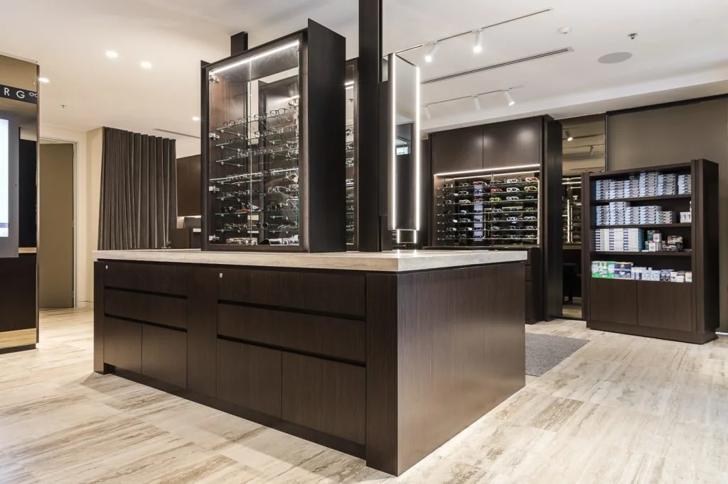 A modern retail display area with glass cases and shelves filled with sunglasses and model cars, powered by ambient and accent lighting.