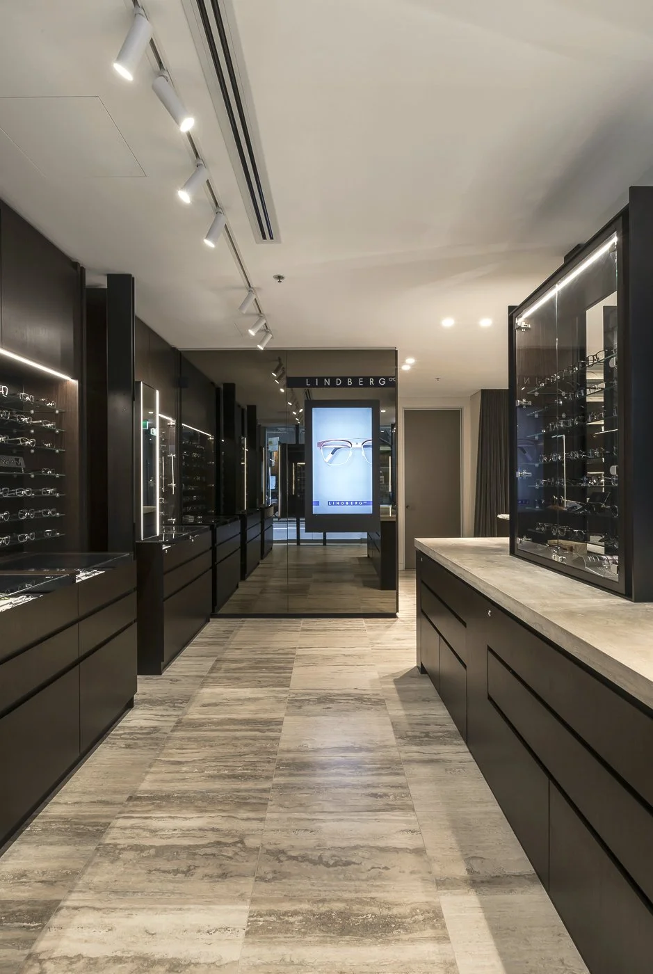 Interior of a modern eyewear store with display cases filled with glasses, black cabinetry, and a digital advertisement display for Lindberg eyewear.