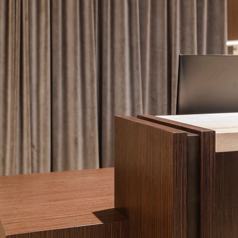 Close-up of a modern reception desk with wood paneling and a marble top, set against a backdrop of beige curtains.