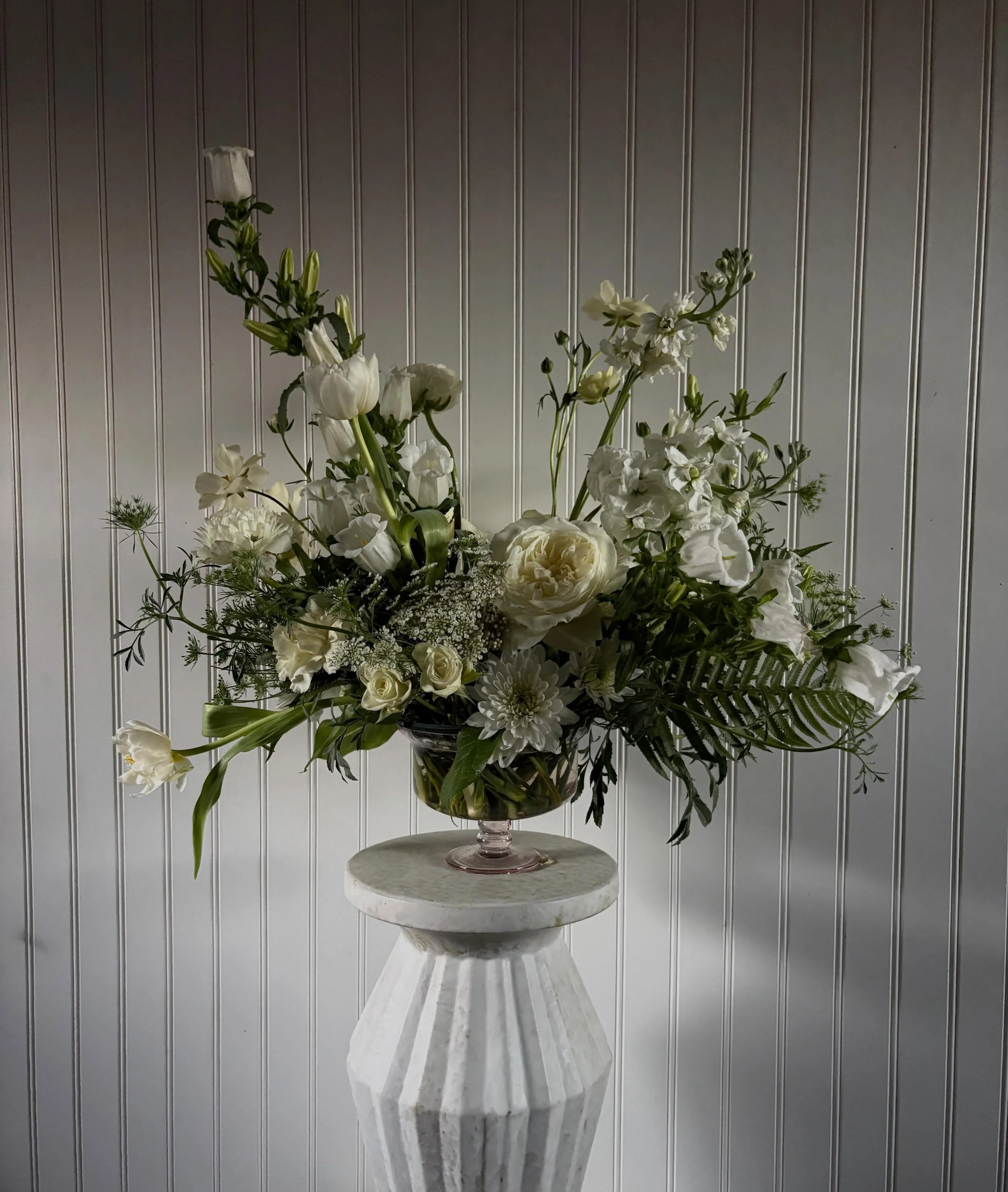 All white blooms with natural foliage from the flowers and a fern.