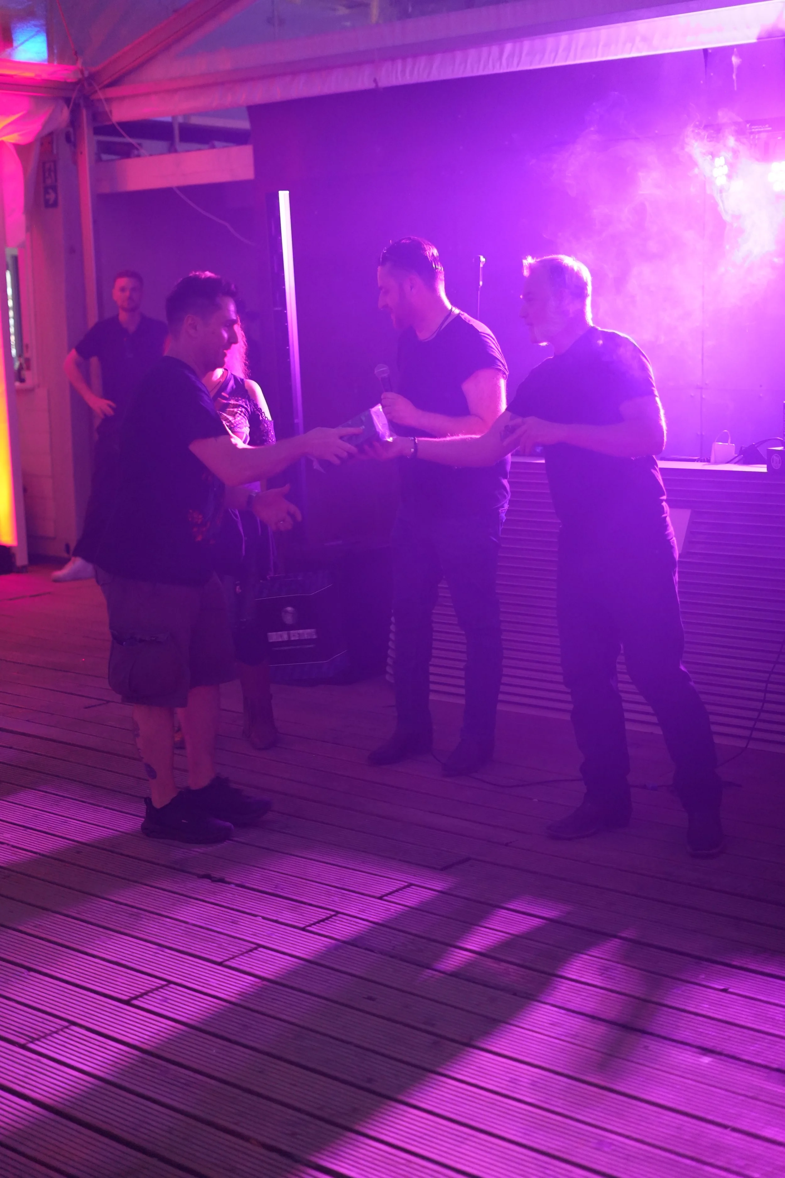 People exchanging gifts or items at a dimly lit event with purple lighting.