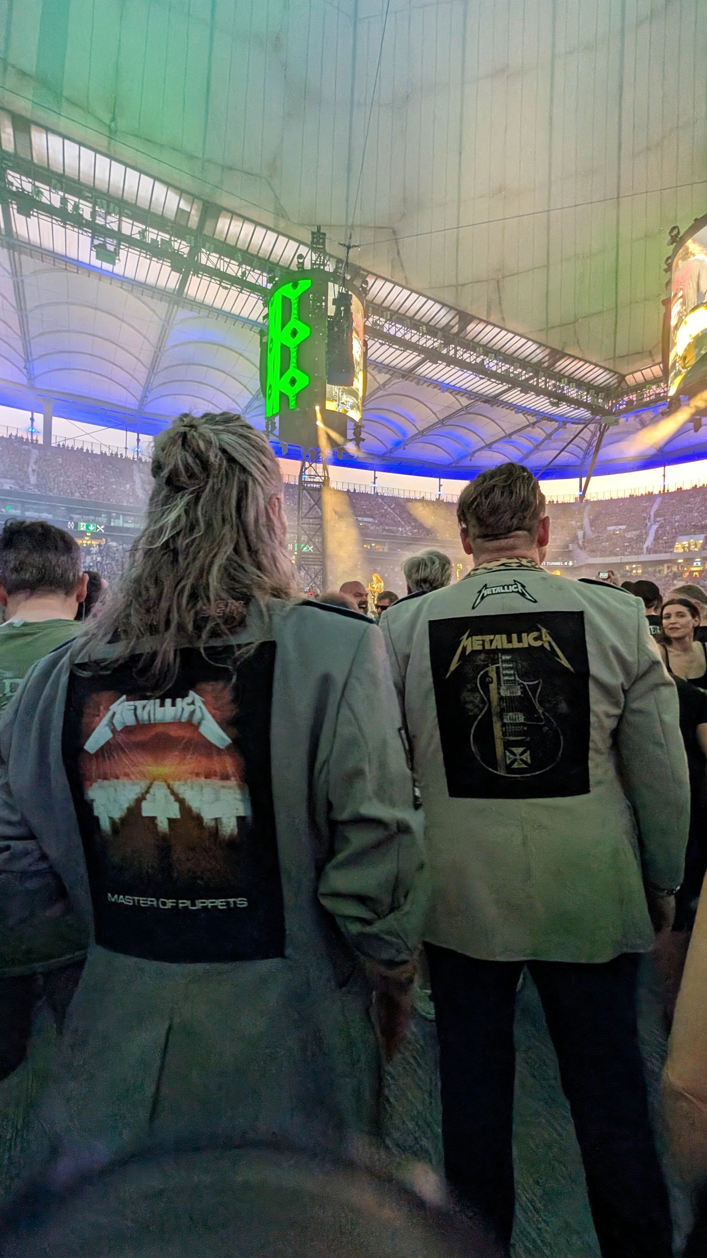 People attending a Metallica concert in a large indoor stadium, with visible security and stage lights.