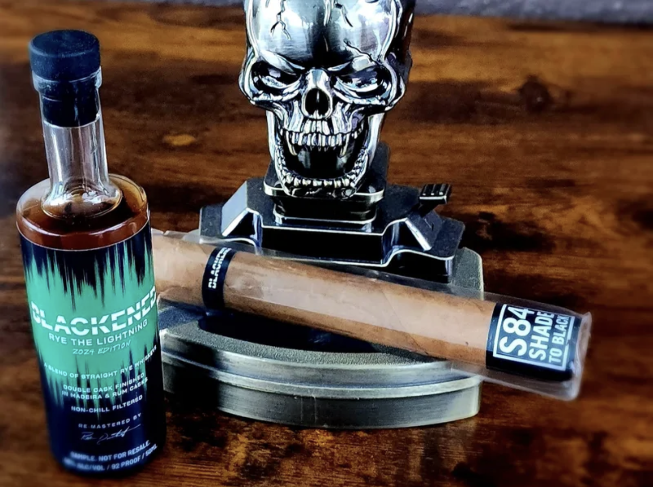 bottle of blackened whiskey with blackened cigar resting on skull ashtray
