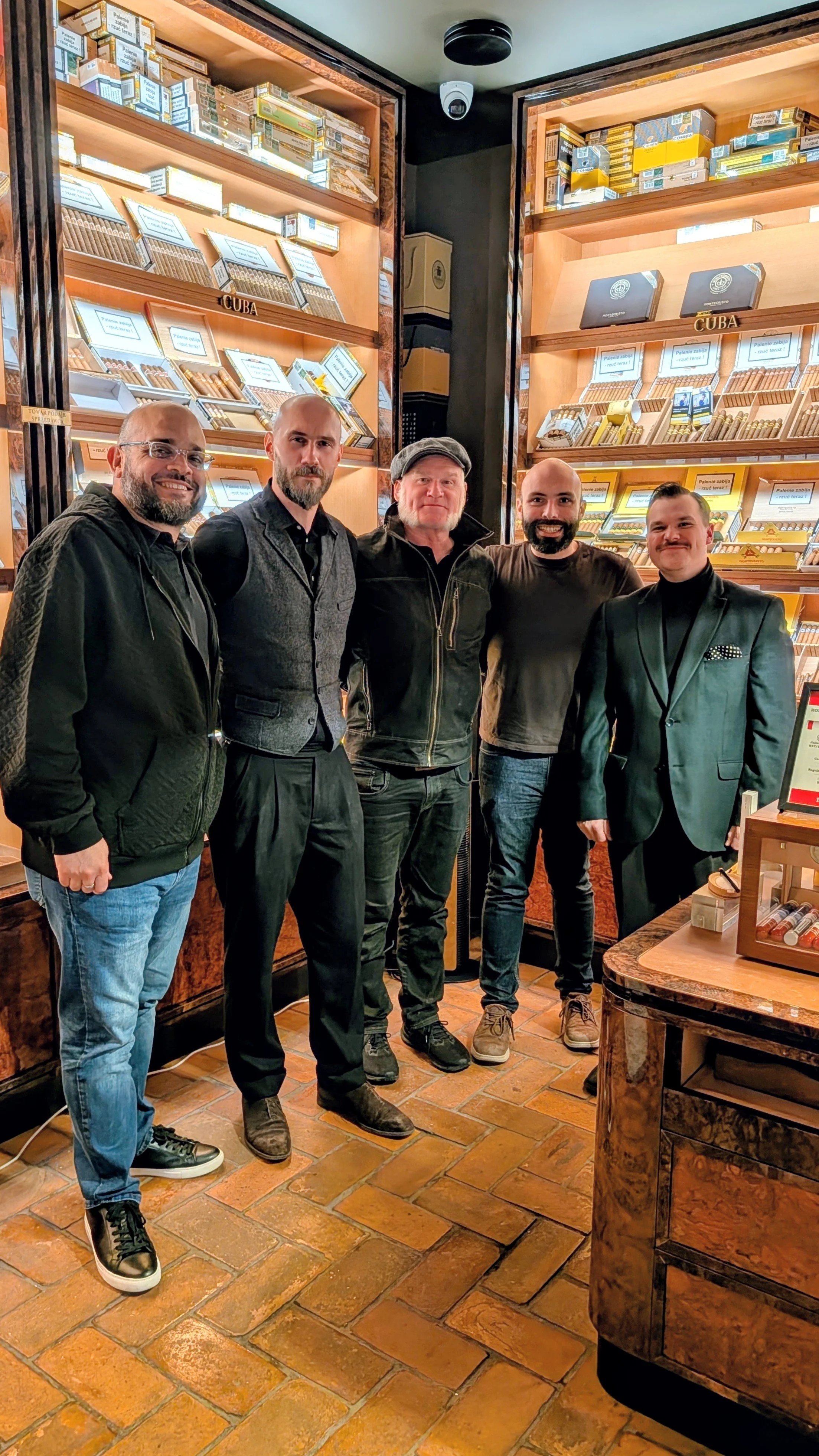 Five men standing inside a cigar shop with shelves of cigars behind them, posing for a group photo.