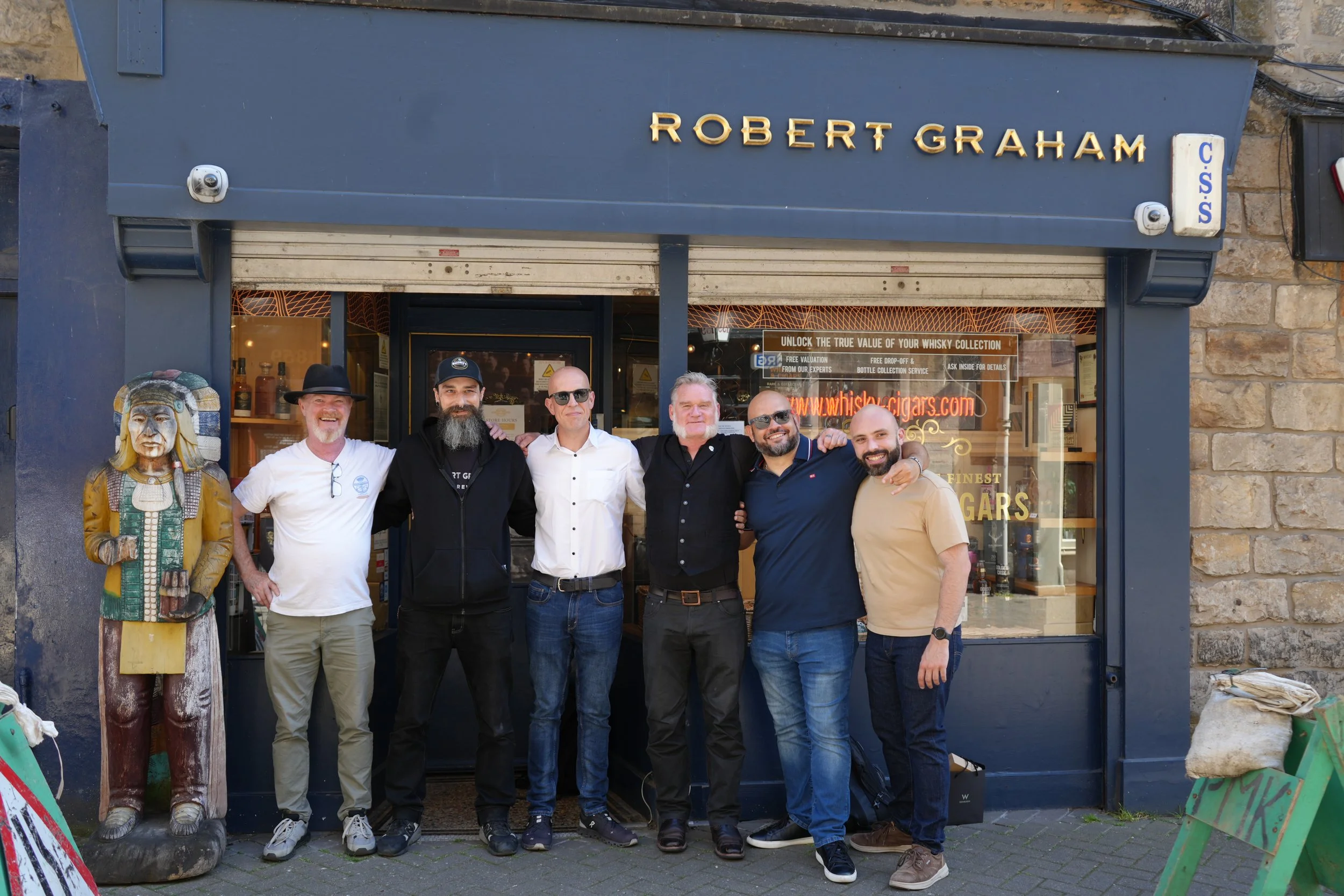 Group of six men standing outside a store named Robert Graham, smiling and posing for the photo.