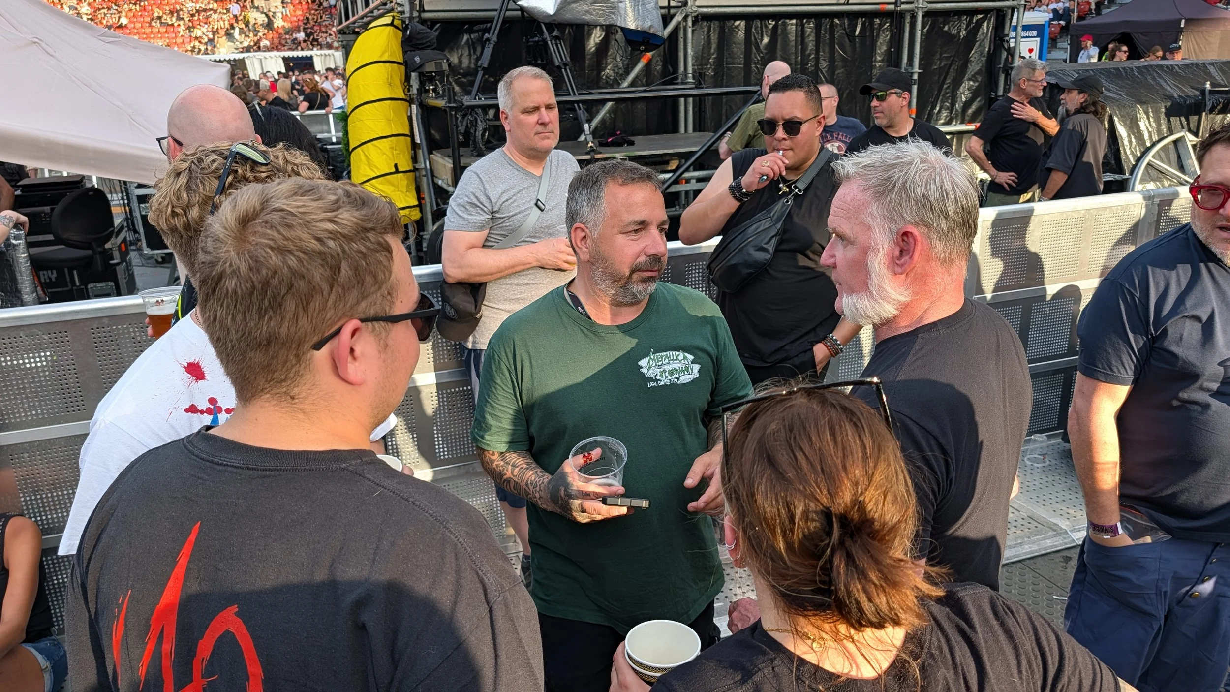 A group of people socializing at a Metallica concert, with some holding drinks, in front of a stage and crowd.