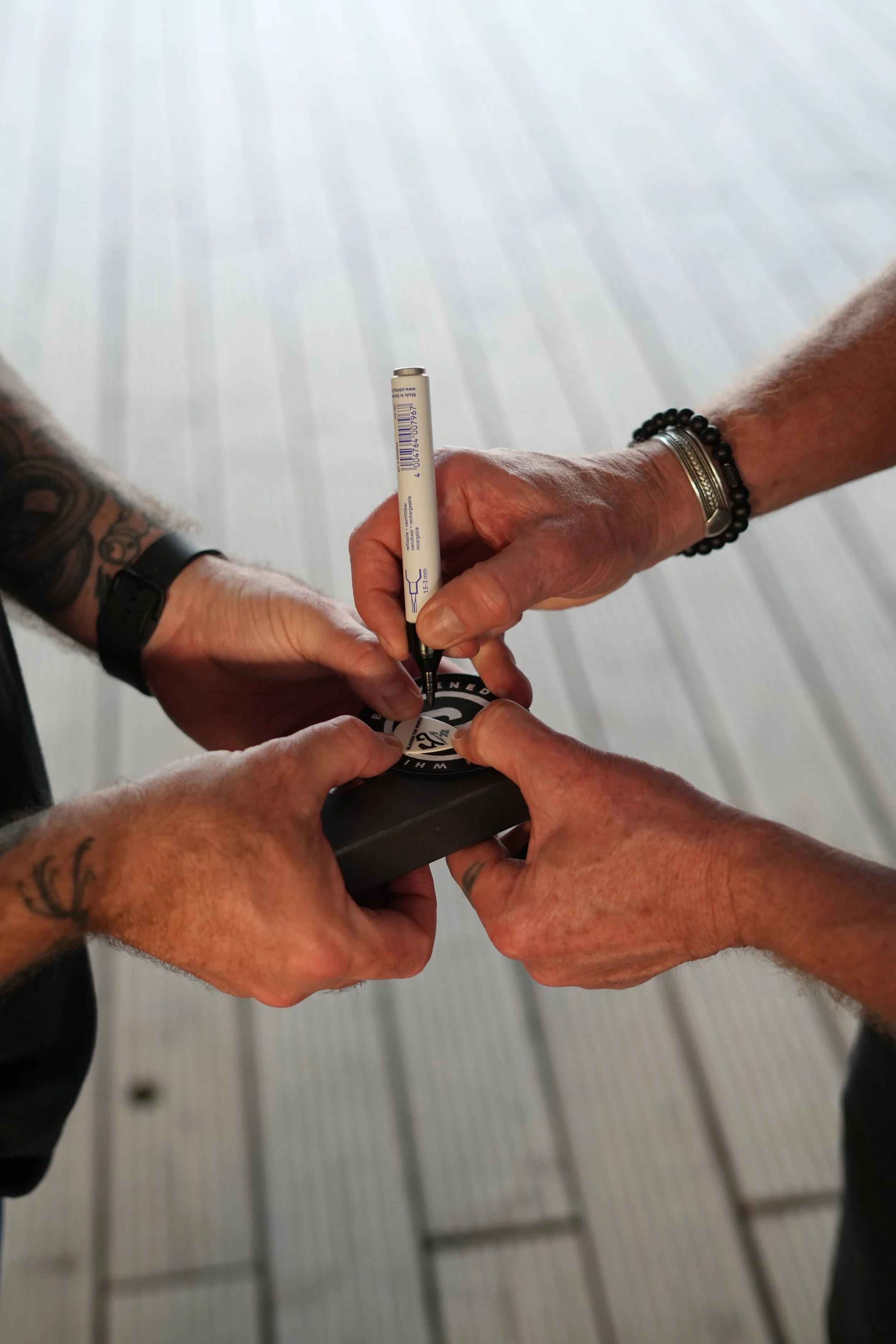 Two individuals exchanging a small sticker, with one using a black pen to sign it.