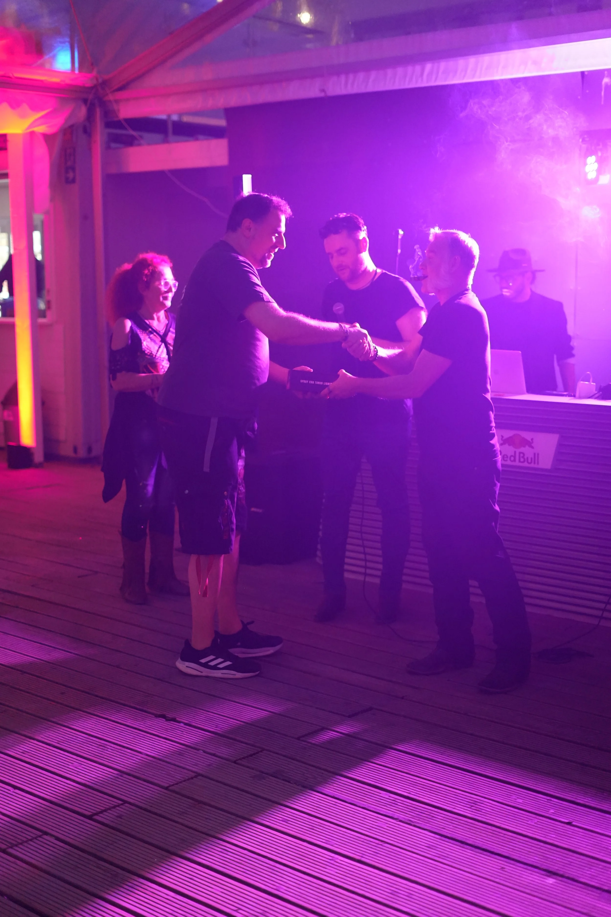 People dancing and enjoying a night at a club with purple lighting and a DJ in the background.