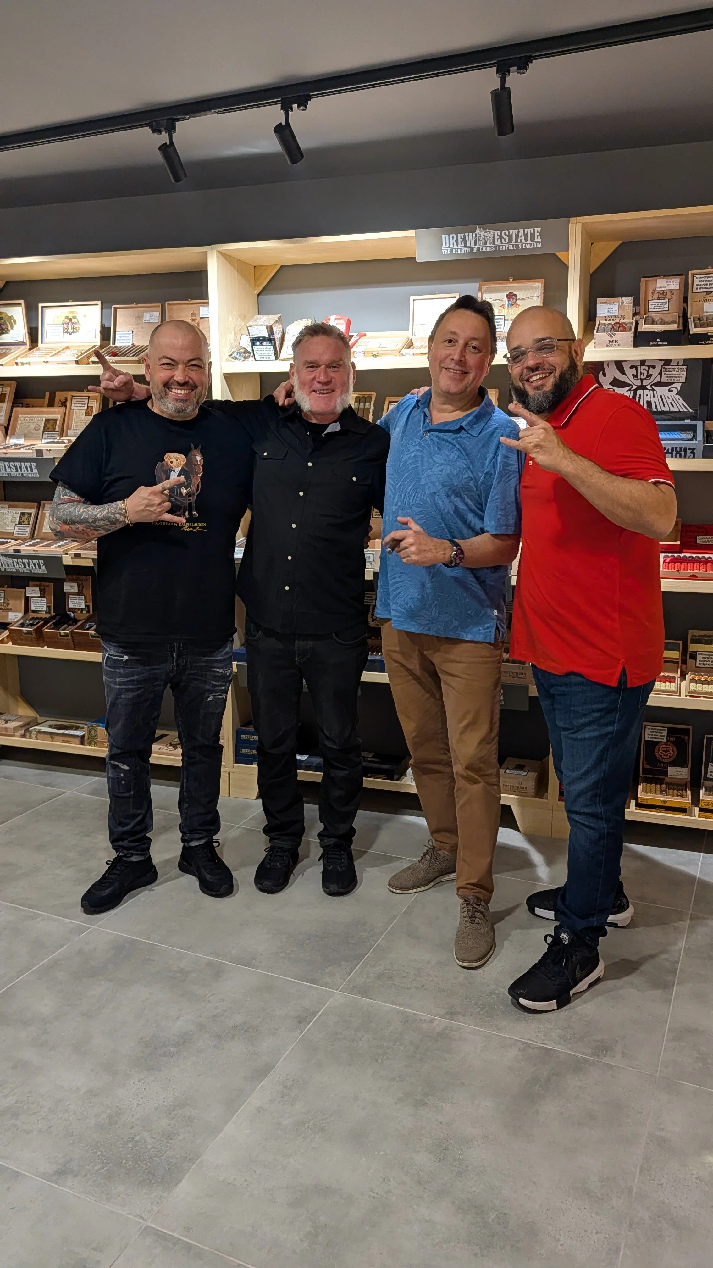 Four men standing in front of a display shelf with pictures and souvenirs, smiling and posing for the camera.