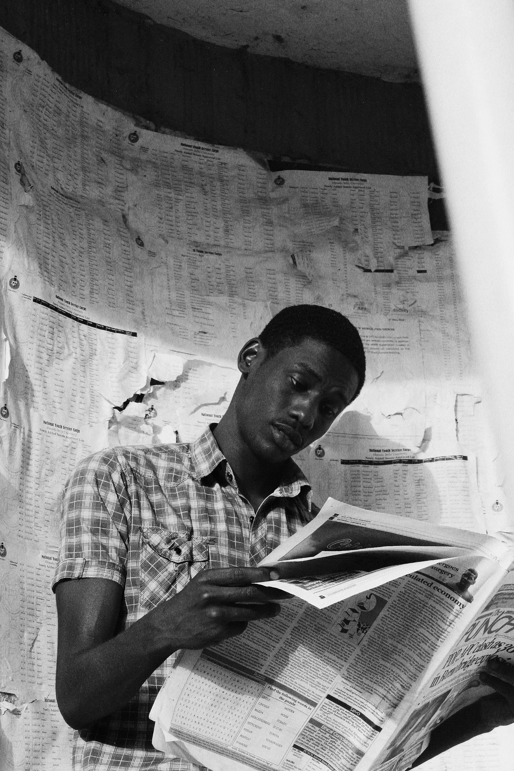 Man reading a newspaper in front of a wall covered with documents.