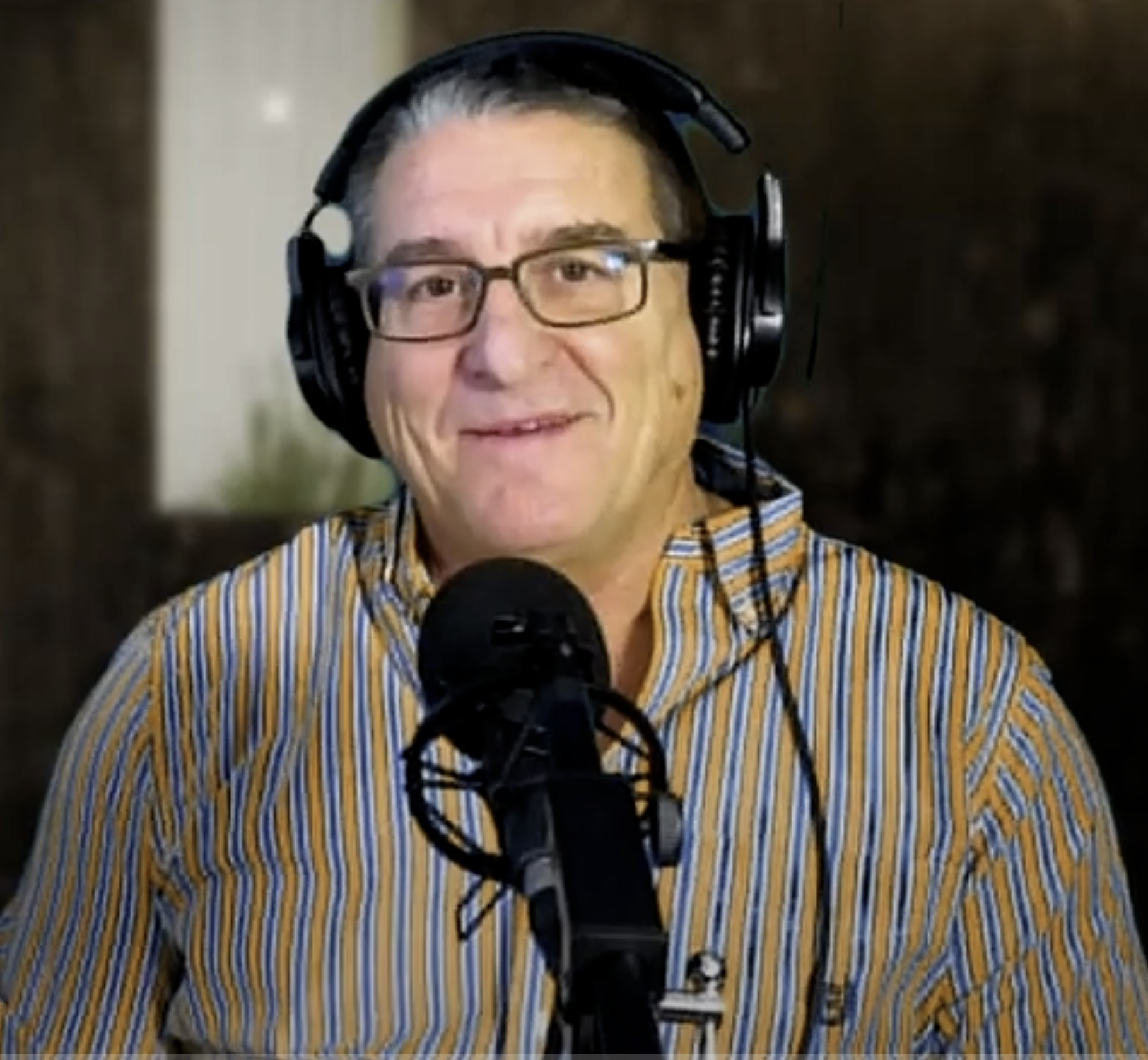Man wearing headphones and glasses speaking into a microphone